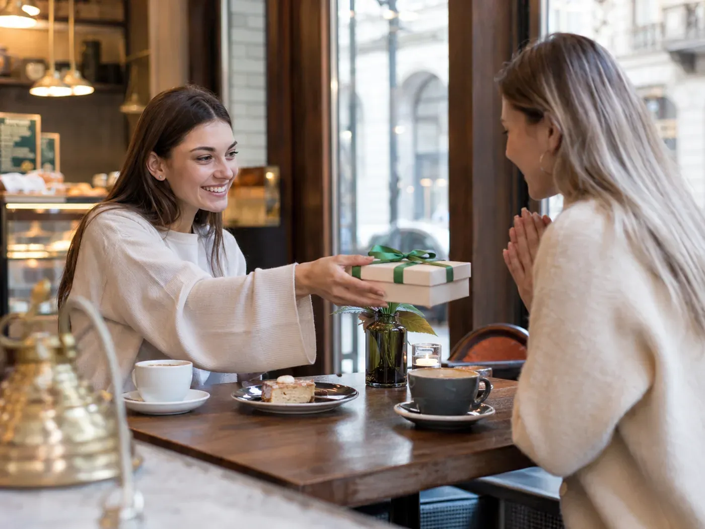 Zwei Freundinnen überreichen sich gegenseitig ein Geschenk in einem Café