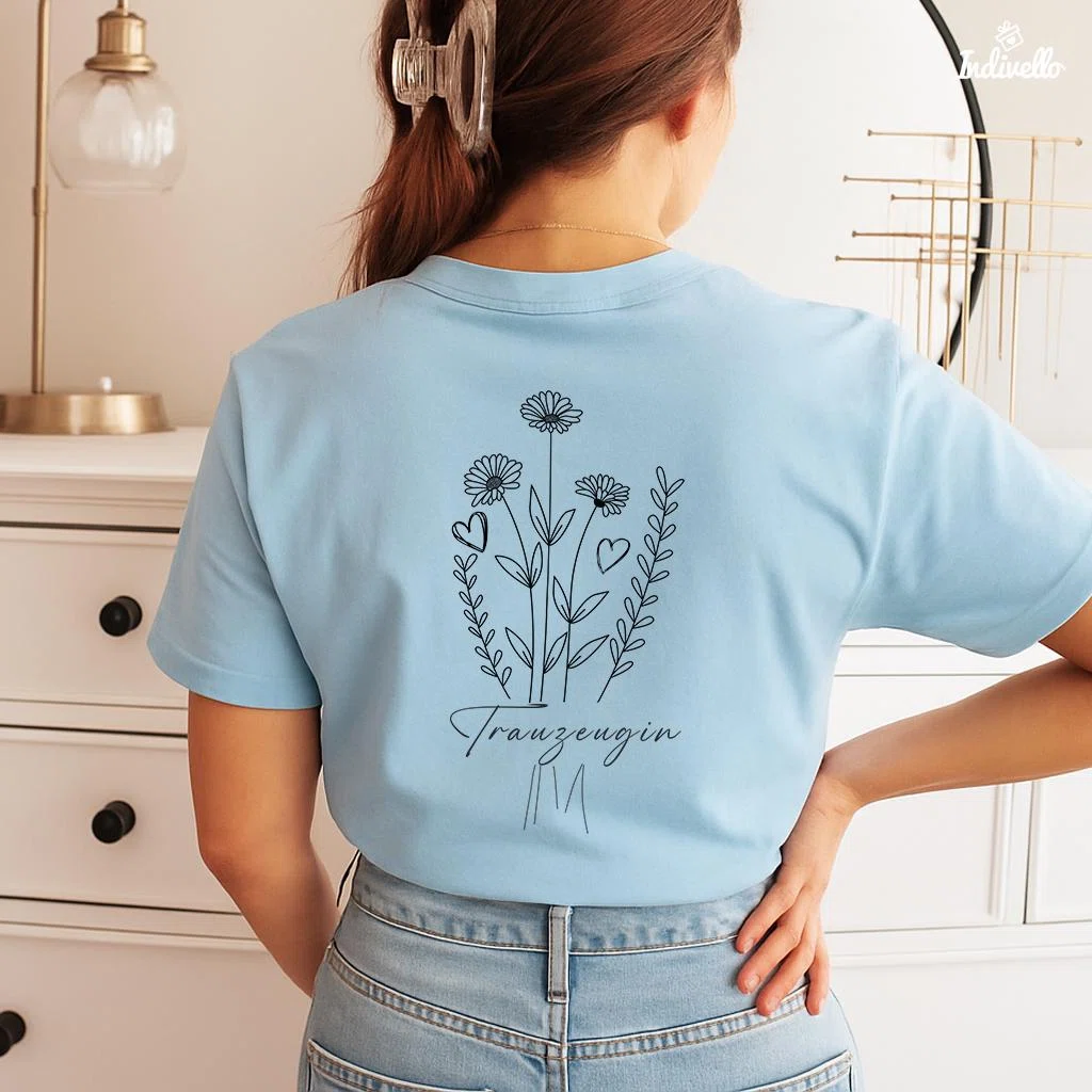 Hellblaues T-Shirt in Rückenansicht mit schwarzer Linienzeichnung aus Blumen, Blättern und Herzen sowie dem Schriftzug „Trauzeugin“.