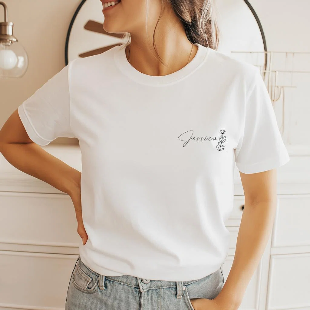 Weißes Kurzarm-T-Shirt in Vorderansicht, links auf der Brust mit einem feinen schwarzen Namen in Schreibschrift und einem kleinen botanischen Zweig bedruckt.