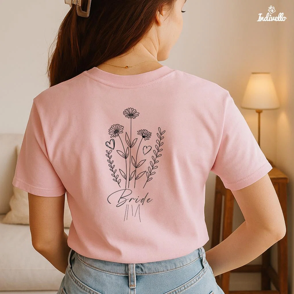 Rosafarbenes Kurzarm-T-Shirt in Rückenansicht, bedruckt mit einer schwarzen Linienzeichnung aus Blumen, Zweigen und Herzen sowie dem Schriftzug „Bride“.