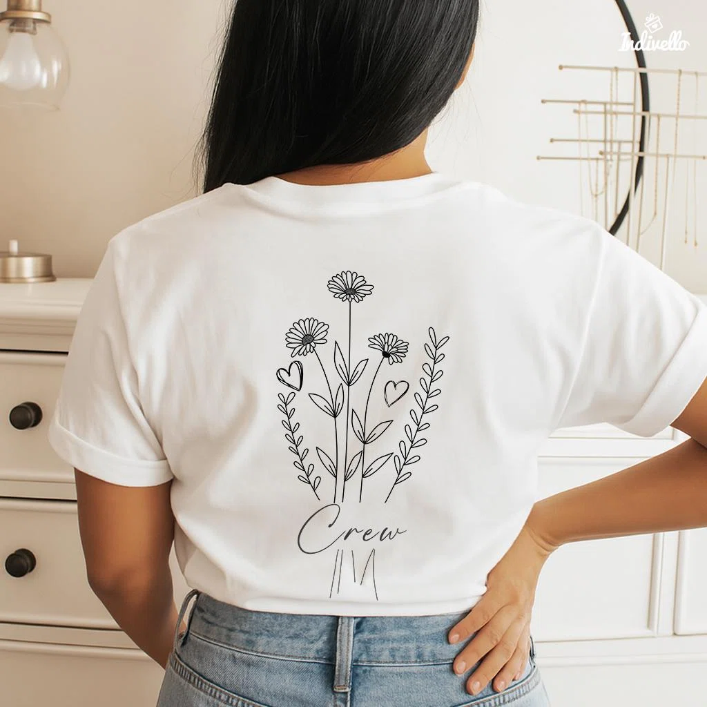 Weißes T-Shirt in Rückenansicht mit schwarzer, filigraner Linienzeichnung aus Margeriten, Blätterzweigen und zwei Herzen; darunter steht „Crew“ in Schreibschrift.