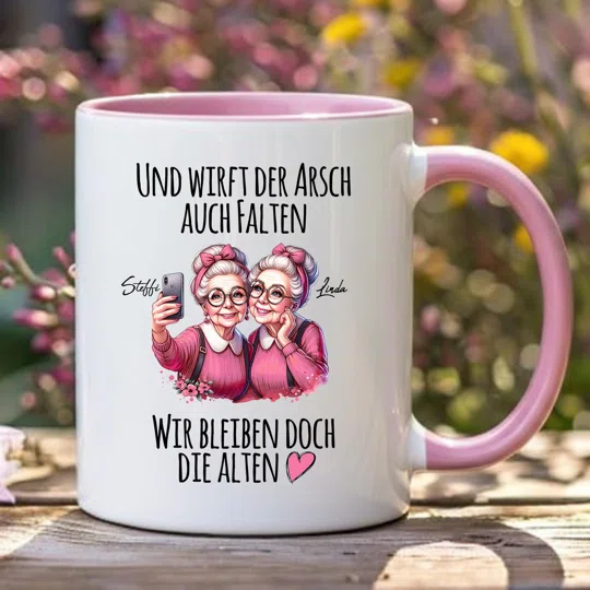 Tasse für Freundinnen kaufen: weiße Tasse mit rosa Innenfläche und Henkel, zwei Comicfiguren beim Selfie und dem Spruch „Und wirft der Arsch auch Falten, wir bleiben doch die Alten“.