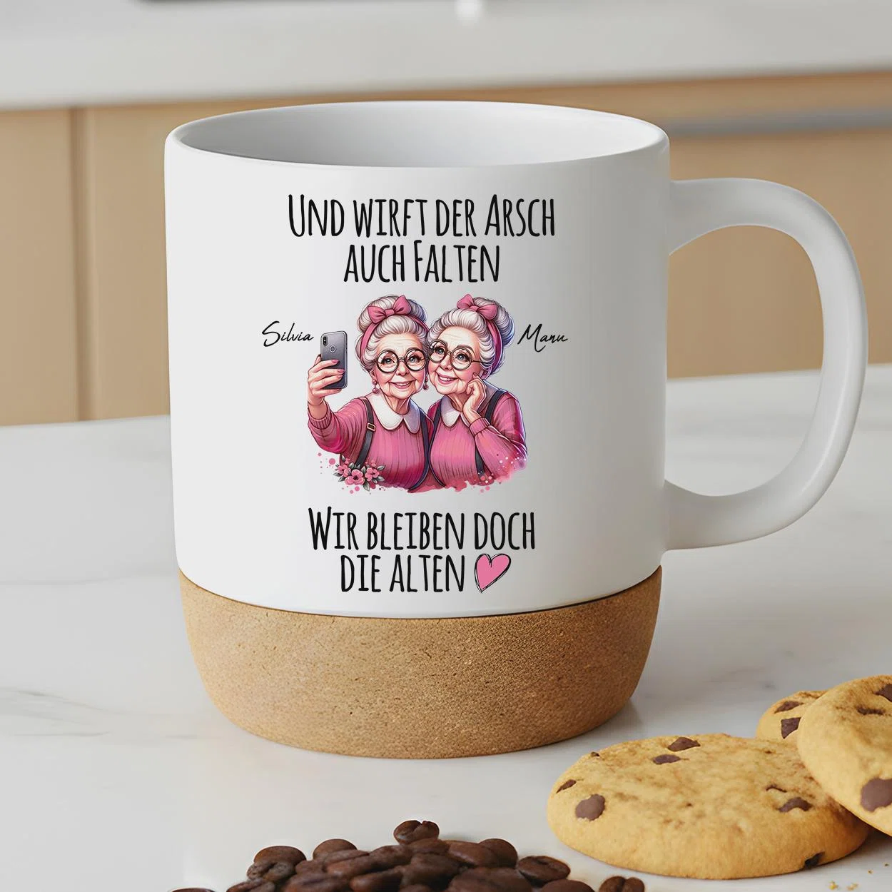 Weiße Tasse mit breitem braunem Sockel und Henkel rechts. Vorn zwei ältere Frauen in Rosa beim Selfie sowie der Spruch „Und wirft der Arsch auch Falten, wir bleiben doch die Alten“ mit Herz.
