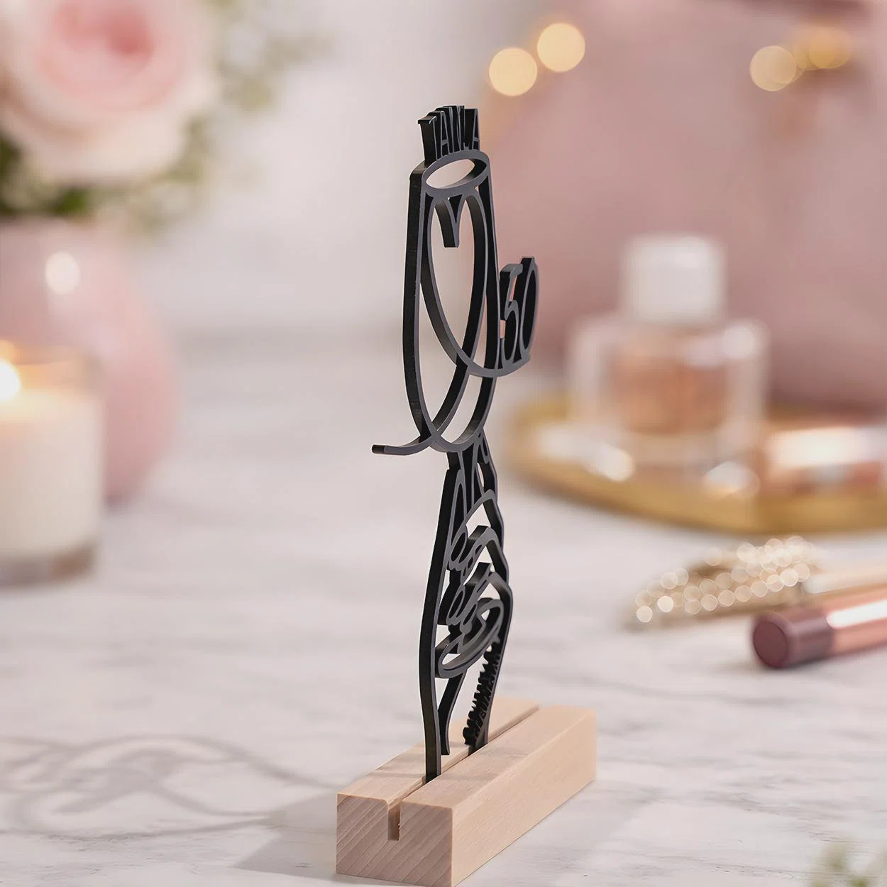Schwarzer, filigran ausgeschnittener Dekostecker mit Schriftzug „MAMA“, großem Herz und Zahl 50, schräg von vorn in einem hellen, rechteckigen Sockel präsentiert.