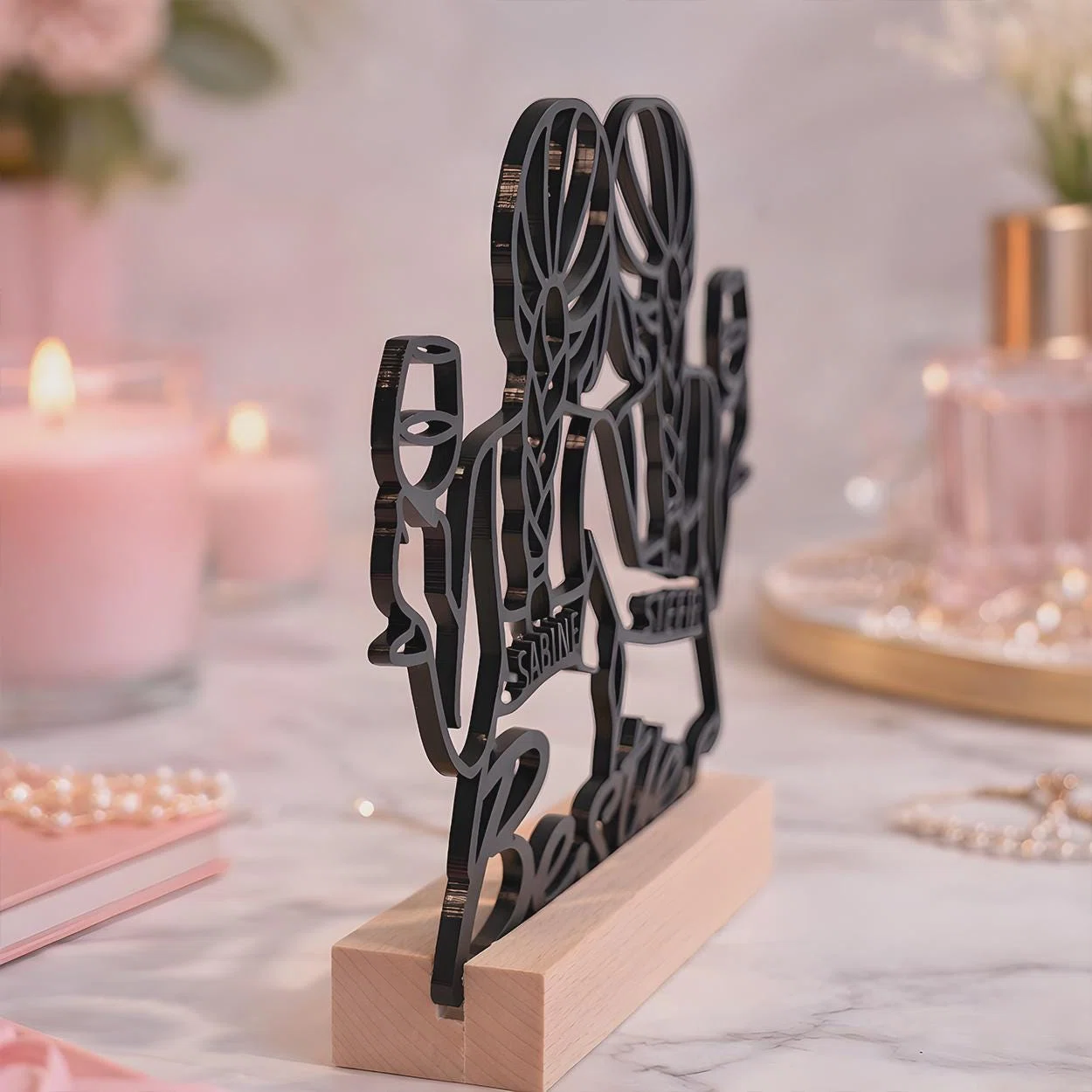 Schwarze, freistehende Silhouetten-Dekoration mit mehreren stilisierten Figuren und integrierten Namen, schräg von der Seite gezeigt in einem hellbraunen Sockel.