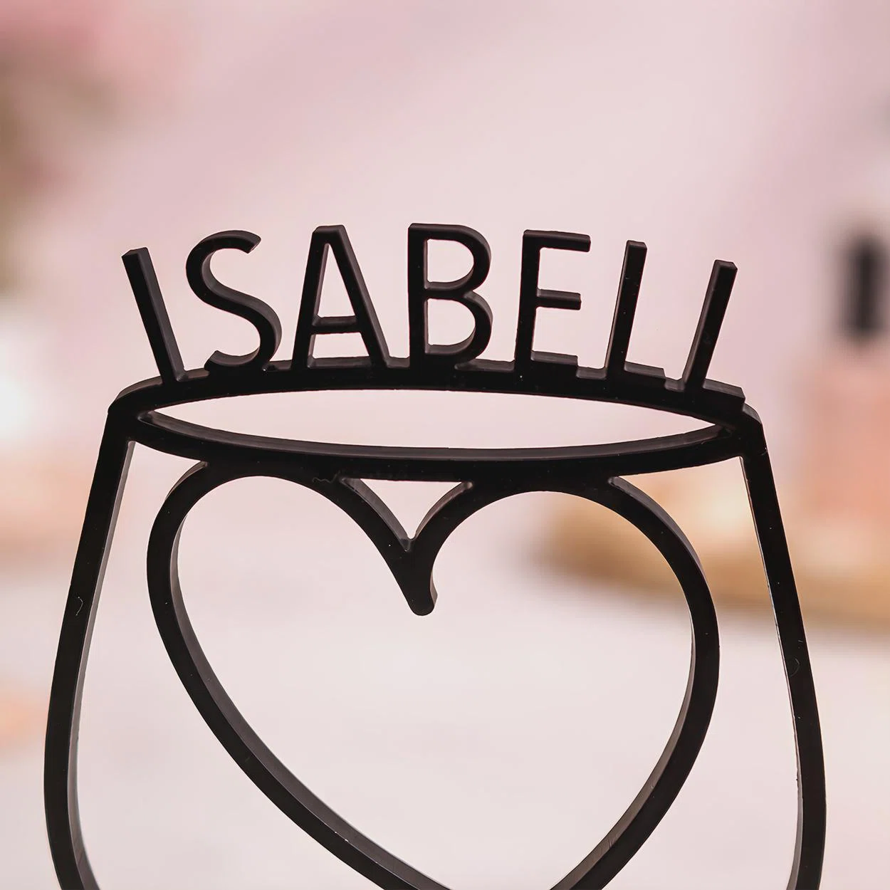 Nahaufnahme eines schwarzen, personalisierten Eierbechers mit großem Herz in der offenen Halterung und dem Namenszug „ISABEL“ am oberen Rand, vor rosafarbenem Hintergrund.