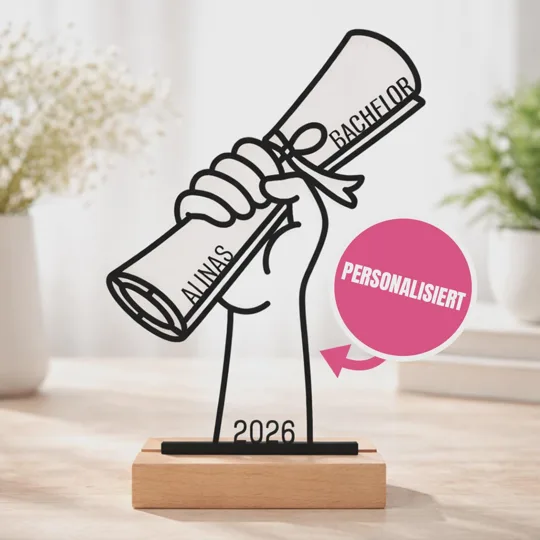 Personalisierten Bachelor-Aufsteller kaufen: schwarze Konturfigur einer Hand mit gerollter Abschlussurkunde, Schleife, Namen und Jahreszahl 2026 auf einem hellen Sockel.