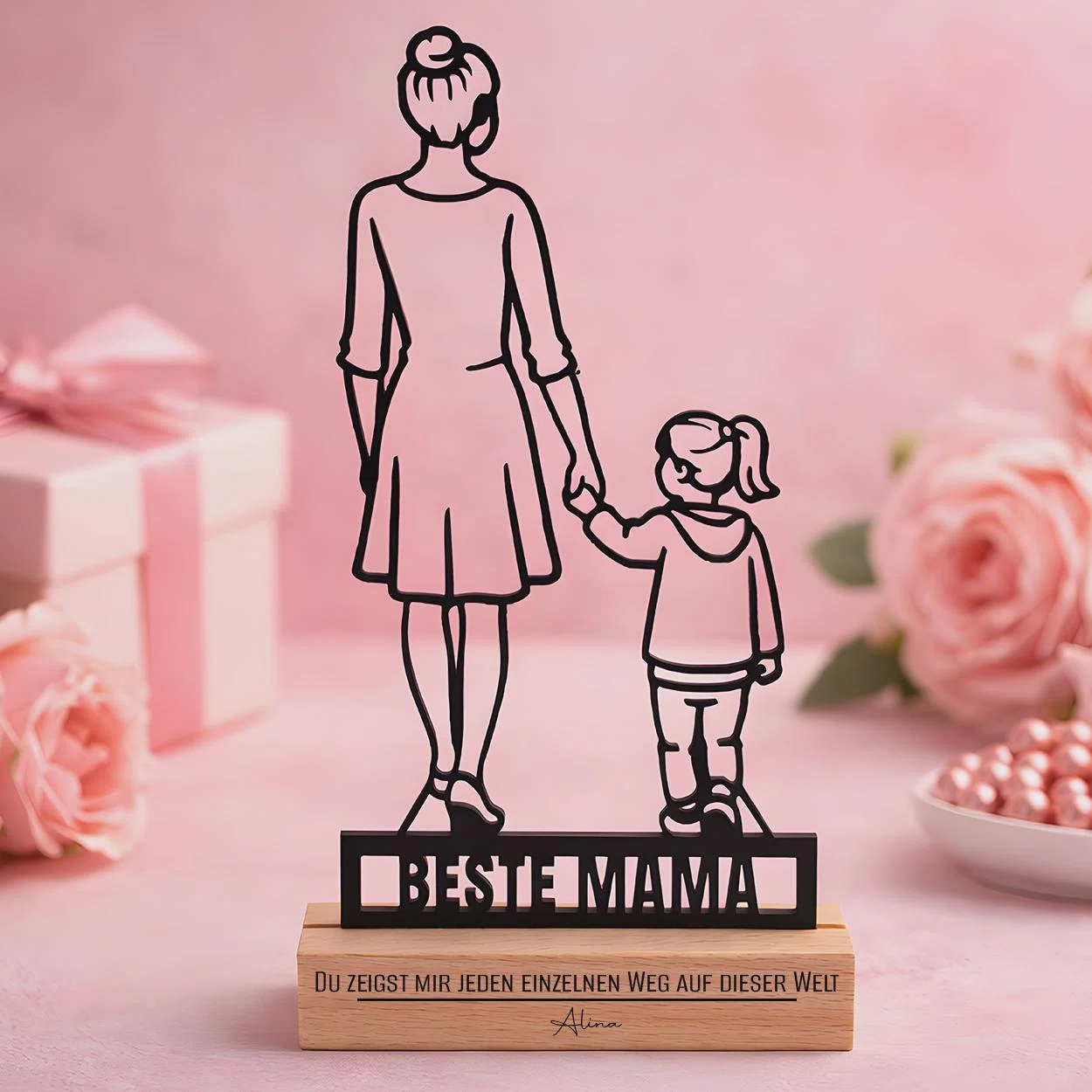 Schwarze Deko-Silhouette einer großen und einer kleinen Figur, die von hinten Hand in Hand dargestellt sind. Darunter stehen „Beste Mama“ und auf dem hellen Sockel „Du zeigst mir jeden einzelnen Weg auf dieser Welt“.