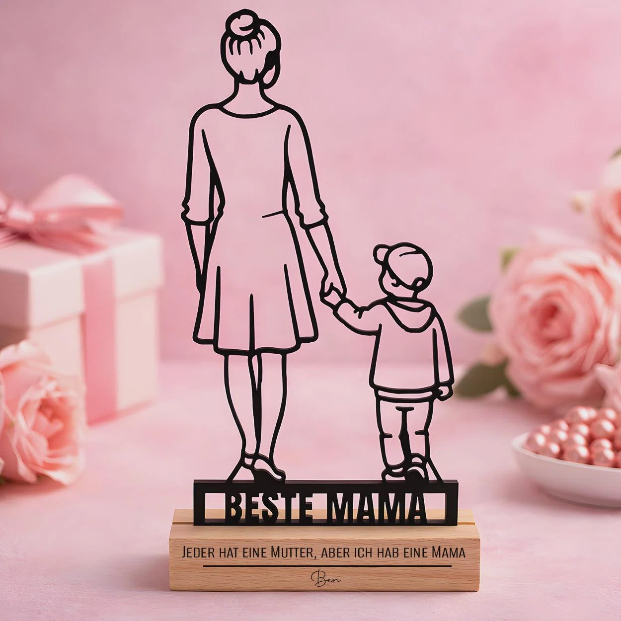Schwarzer Aufsteller mit rückwärtiger Silhouette einer erwachsenen Person und eines Kindes, darunter „BESTE MAMA“. Der hellbraune Sockel trägt den Spruch „Jeder hat eine Mutter, aber ich hab eine Mama“.