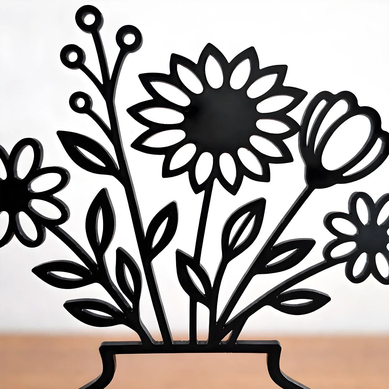 Schwarze, flache Dekoration mit stilisierten Blumen, Knospen und Blättern in durchbrochener Silhouettenform, frontal vor hellem Hintergrund fotografiert.