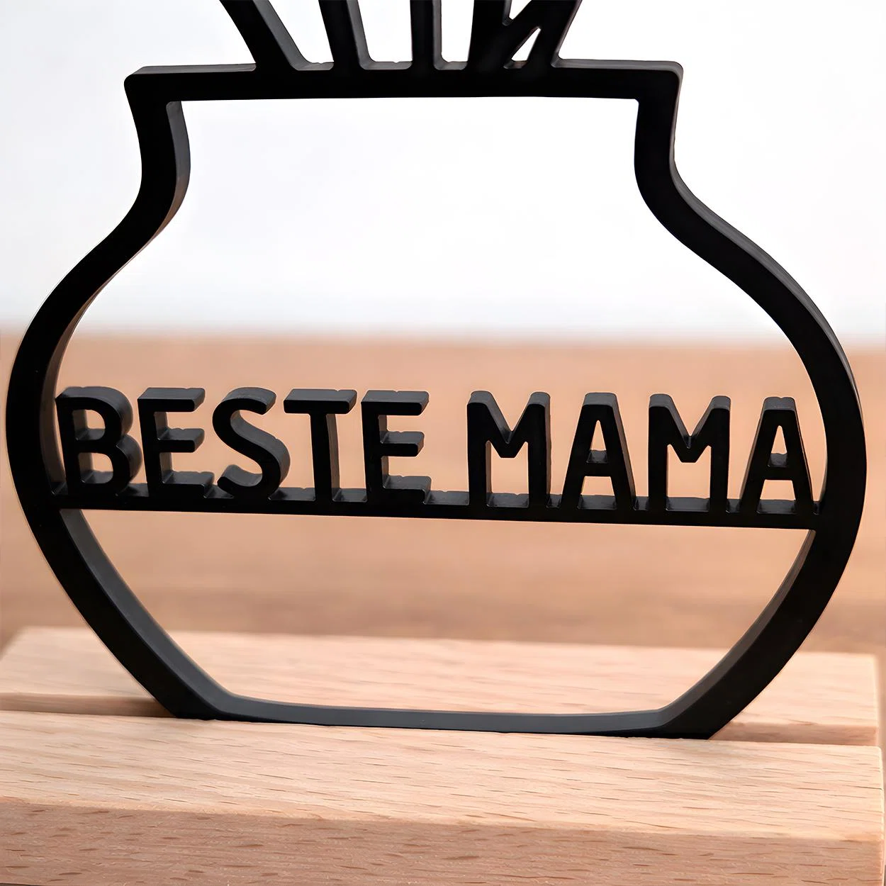 Schwarzer, freistehender Deko-Aufsteller in Vasenform mit der ausgeschnittenen Aufschrift „BESTE MAMA“ und stilisierten Blumen am oberen Rand, frontal auf hellem Holz.