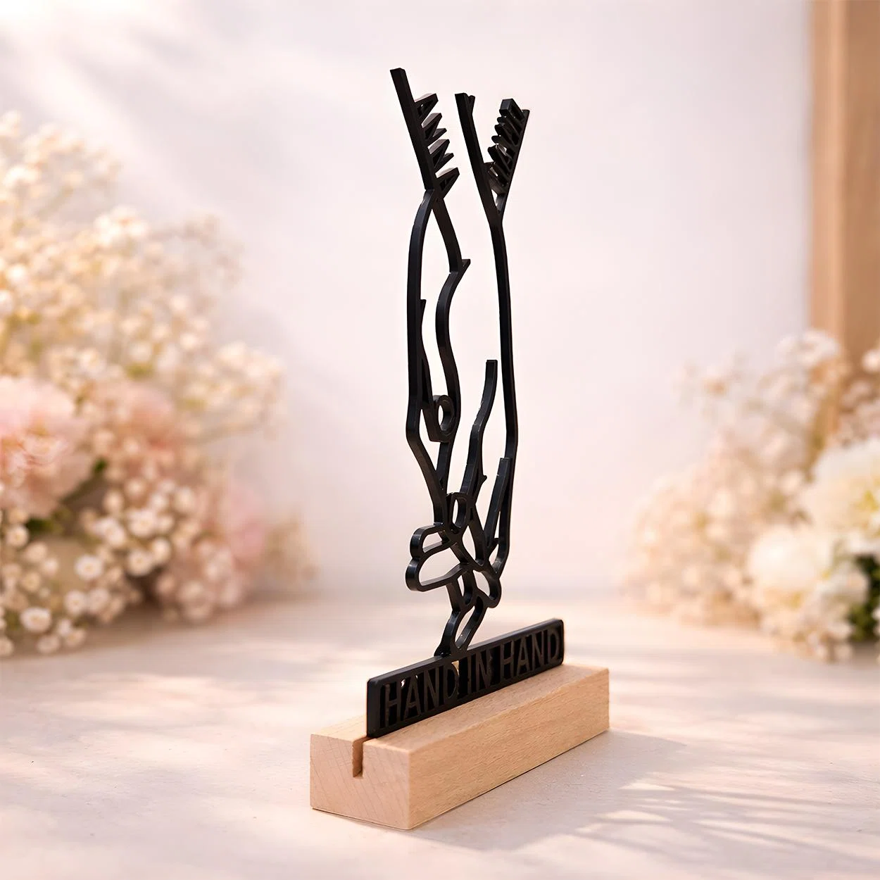 Filigrane schwarze Dekofigur mit der Silhouette zweier ineinandergreifender Hände und dem Schriftzug „HAND IN HAND“, senkrecht in einem hellen Sockel in Holzoptik.