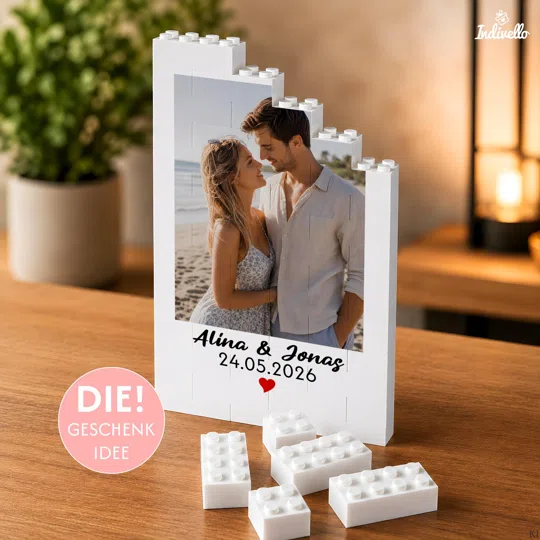 Fotogeschenk zum Jahrestag personalisiert kaufen: weißer Klemmbaustein-Aufsteller mit stufigem Rand, Paarfoto, Namen, Datum und rotem Herz; lose Bausteine liegen davor.