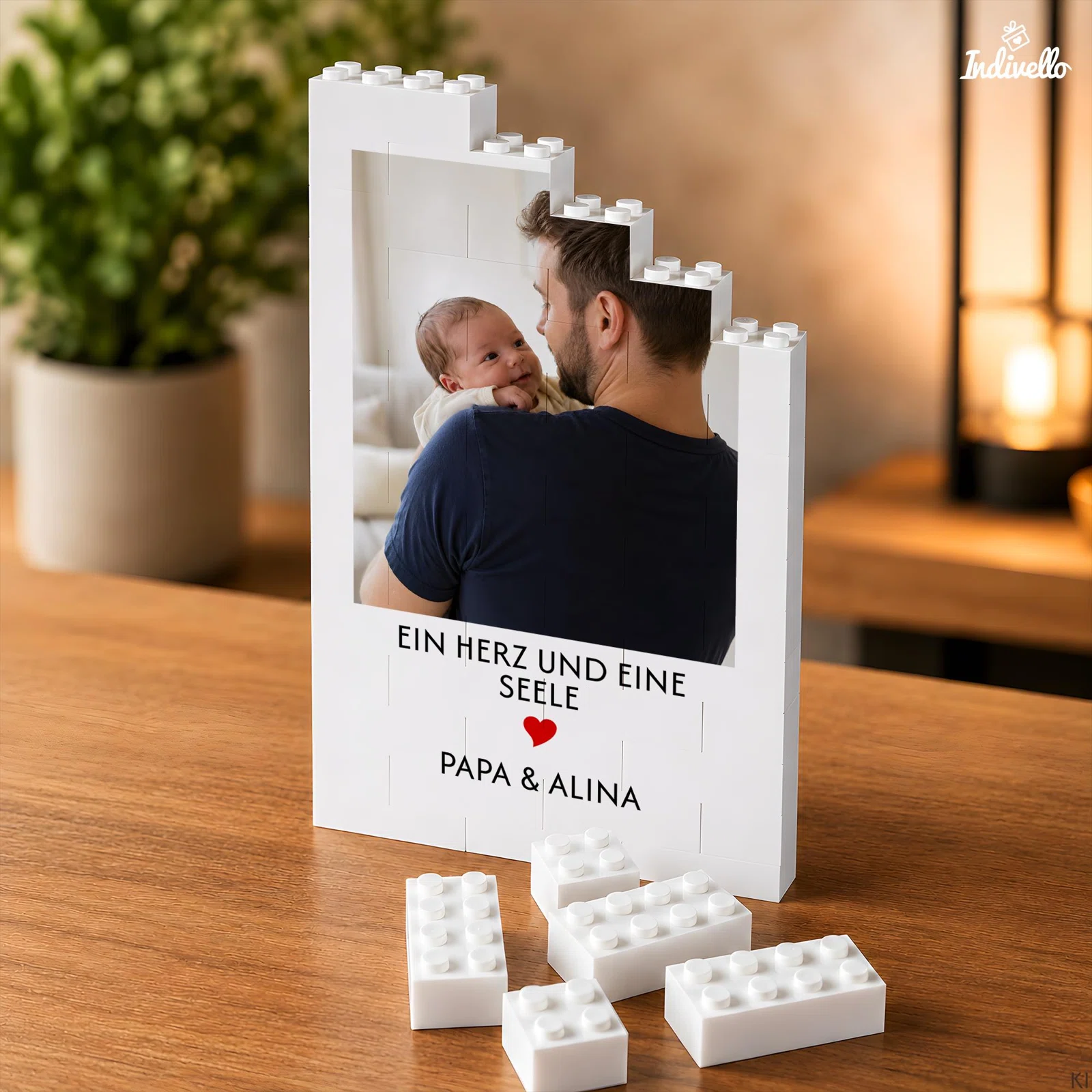 Weißer Bilderrahmen in Klemmbaustein-Optik mit Foto einer erwachsenen Person und eines Babys, rotem Herz und Spruch „Ein Herz und eine Seele“. Lose weiße Bausteine liegen davor.