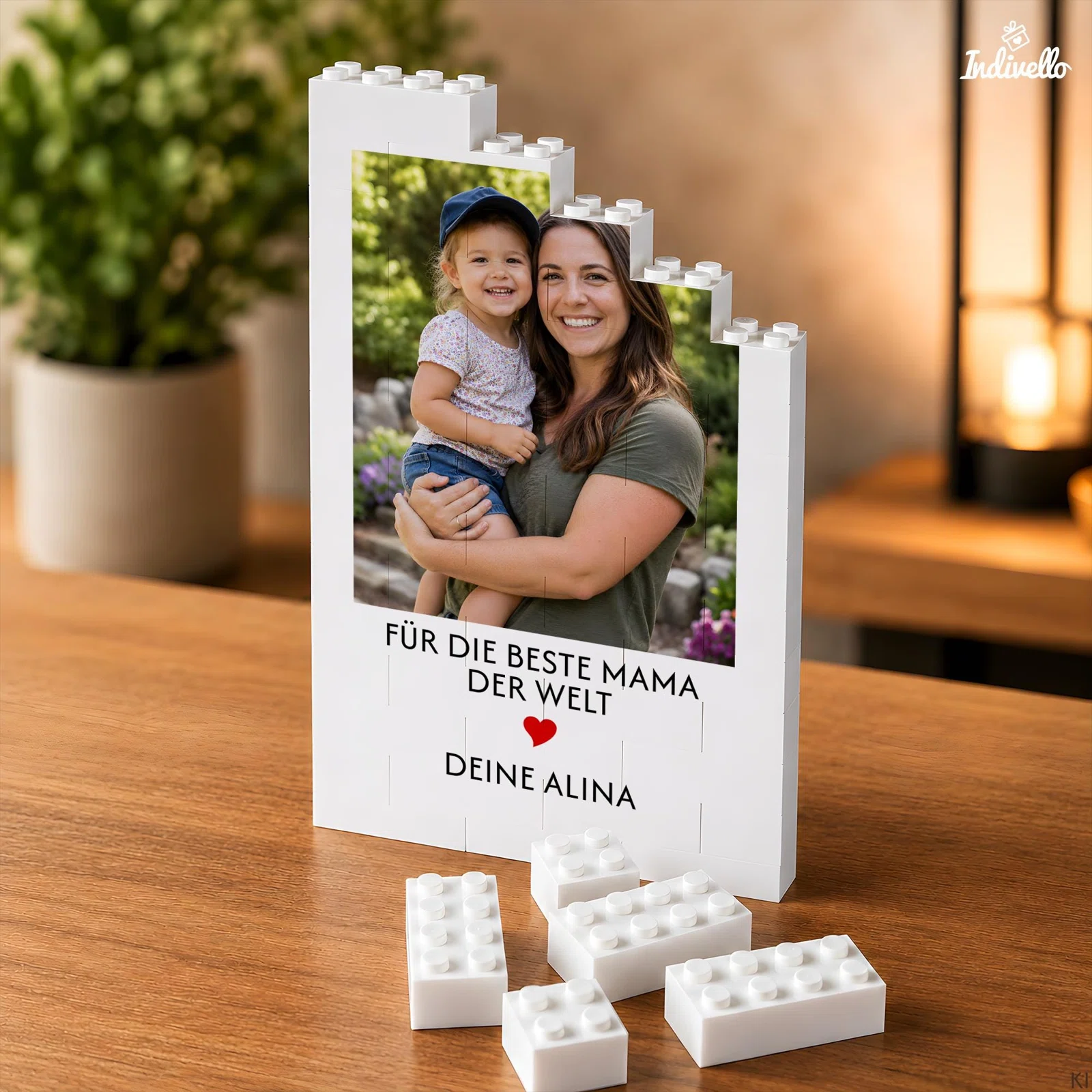 Weißer, hochformatiger Fotohalter in Bausteinoptik mit stufenförmigem Rand, persönlichem Foto, Widmung für Mama und rotem Herz. Mehrere lose weiße Bausteine liegen davor auf dem Holztisch.