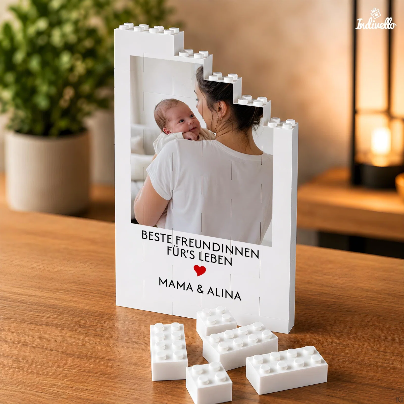 Weißer, stufenförmiger Fotorahmen in Bausteinoptik mit dem Foto einer erwachsenen Person und eines Babys. Darunter stehen ein Freundinnen-Spruch, ein rotes Herz und Beispielnamen.