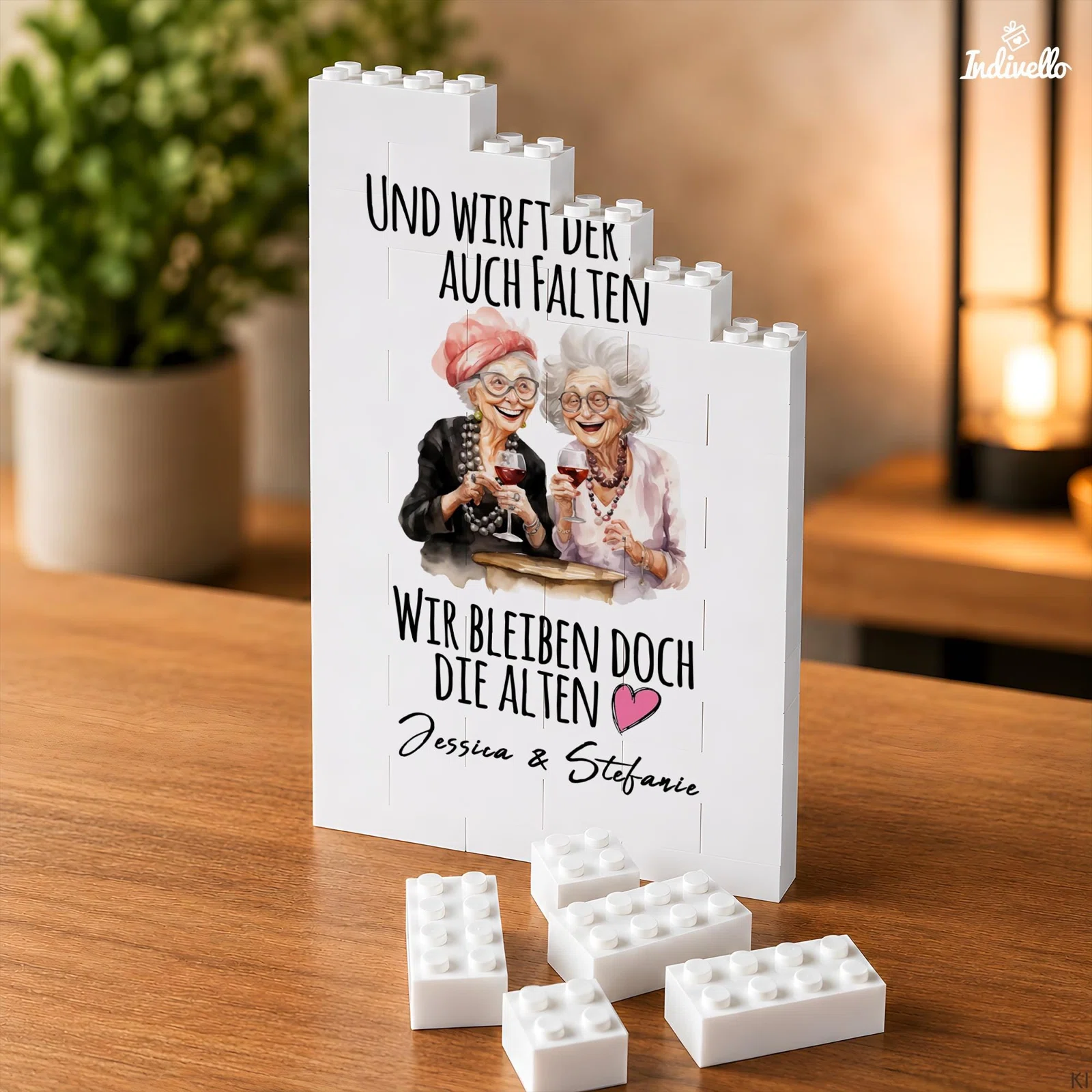 Aufrecht stehendes Puzzle aus weißen Klemmbausteinen mit Illustration zweier älterer Frauen mit Weingläsern. Dazu der Spruch „Und wirft der auch Falten, wir bleiben doch die Alten“ samt Namen und rosa Herz.