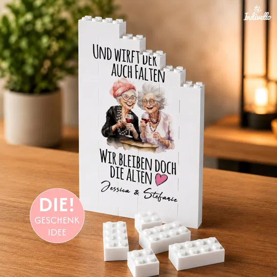 Personalisiertes Freundinnen-Geschenk bestellen: weiße Klemmbaustein-Tafel mit stufiger Oberkante, zwei illustrierten Frauen beim Anstoßen, humorvollem Spruch und Namen.