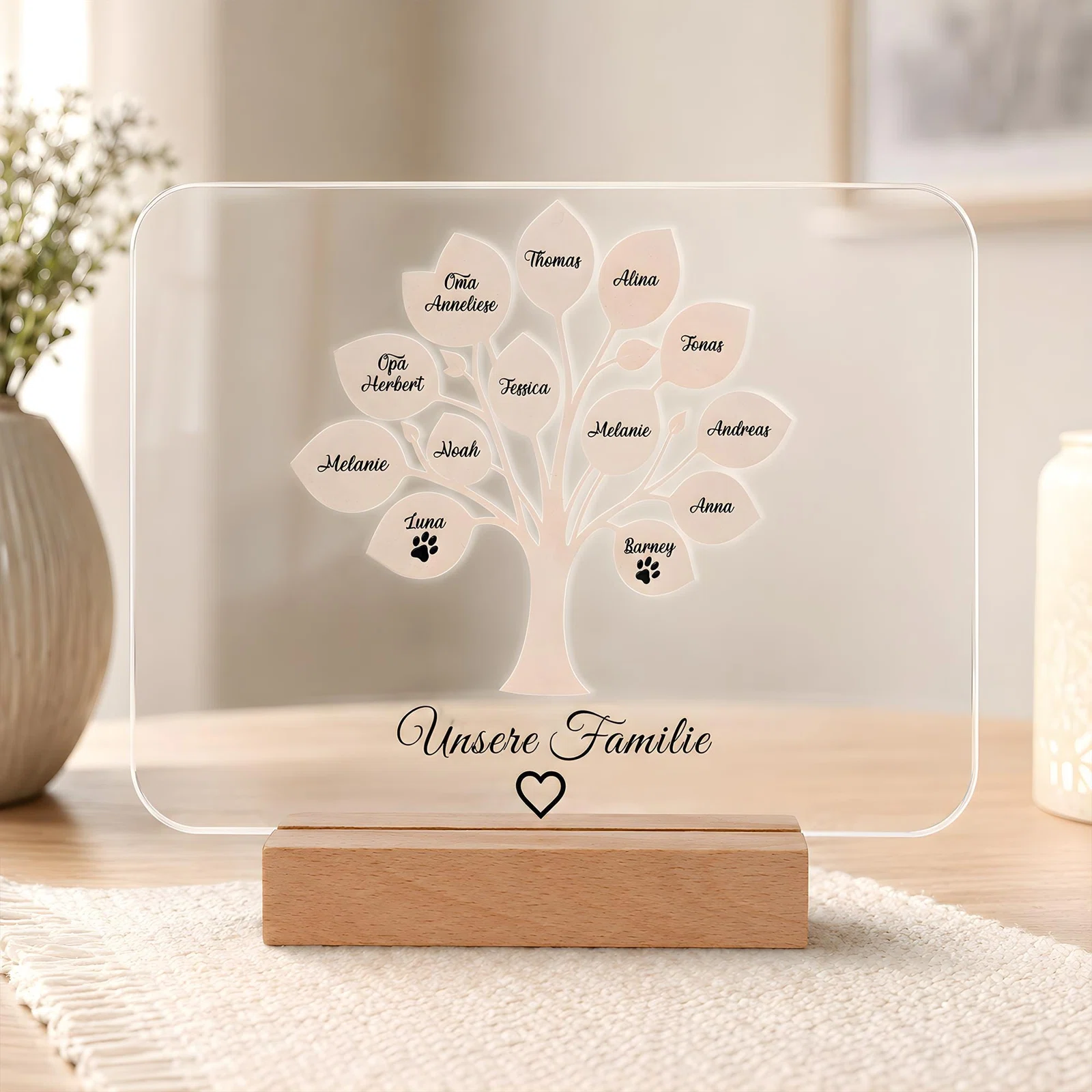 Transparente, abgerundete Tafel im holzfarbenen Sockel, frontal fotografiert. Ein weißer Stammbaum mit beschrifteten Blättern und Pfotenmotiven steht über „Unsere Familie“ samt Herz.
