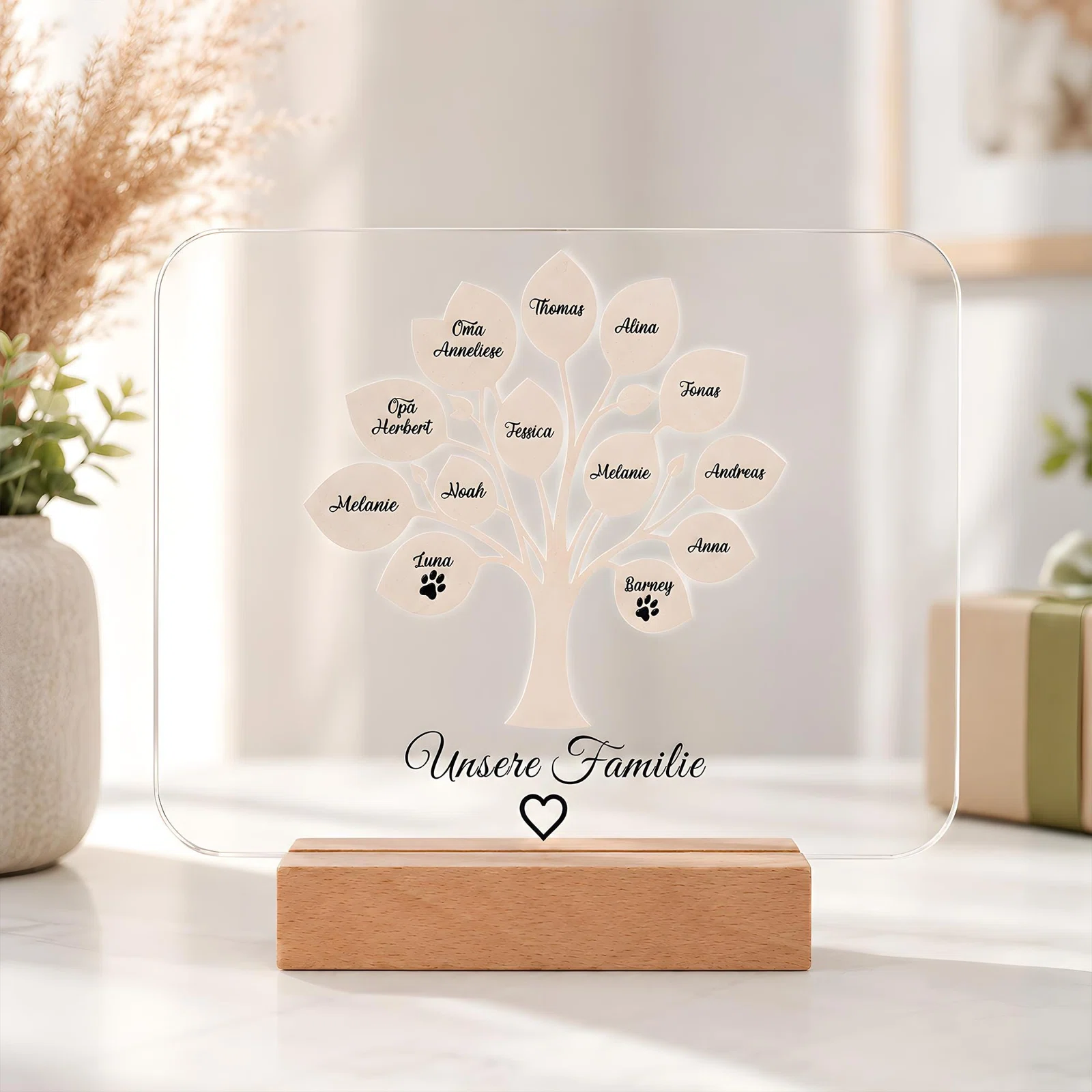 Transparente, abgerundete Namenstafel im Holzsockel, frontal fotografiert. Ein heller Stammbaum trägt personalisierte Blätter und zwei Pfoten; darunter stehen „Unsere Familie“ und ein Herz.