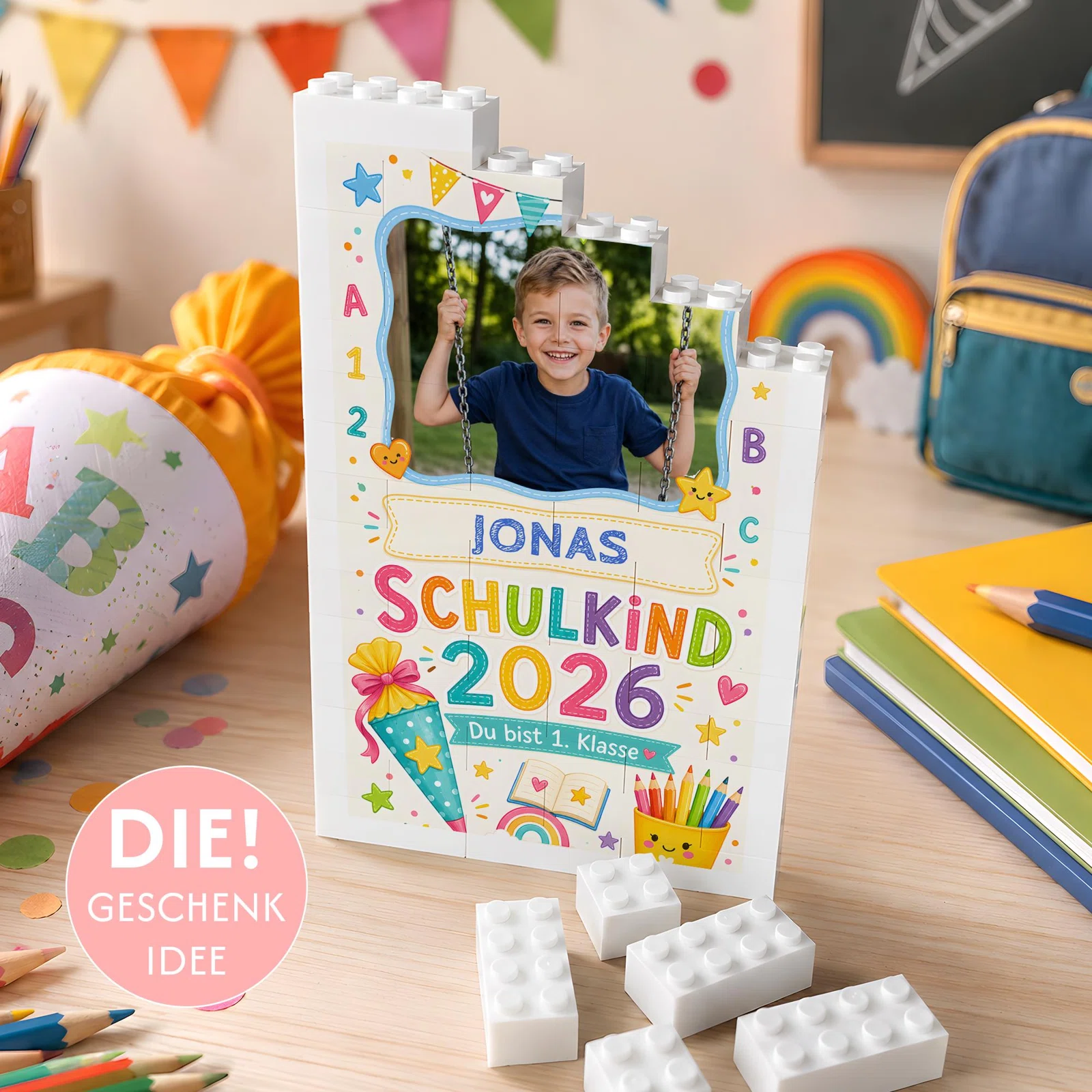 Fotogeschenk zur Einschulung bestellen: weißer Baustein-Aufsteller mit Kinderfoto, bunten Schulmotiven, Name sowie „Schulkind 2026“ und „Du bist 1. Klasse“.