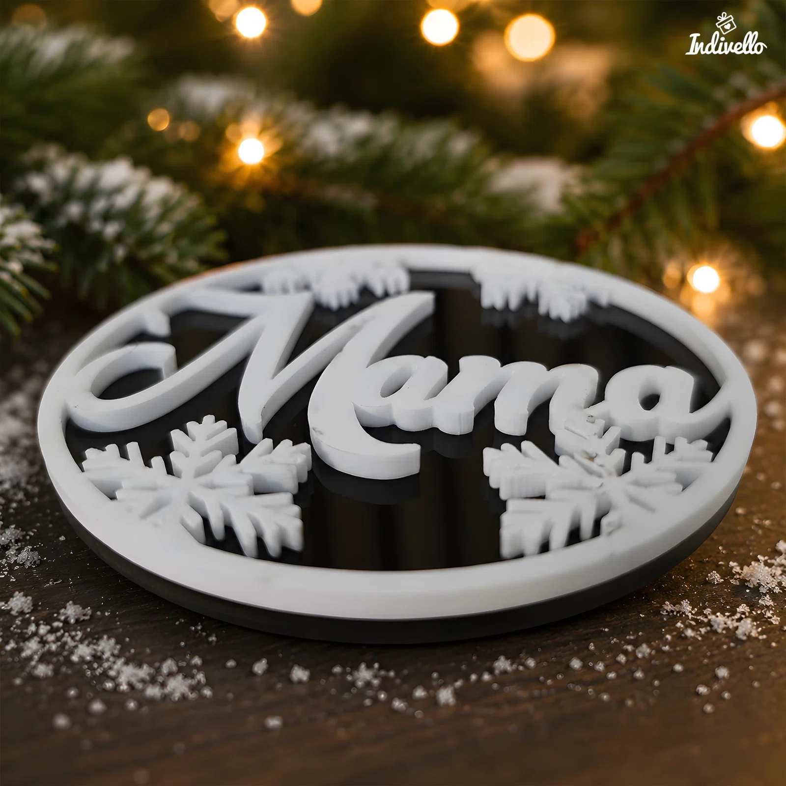 Runder Anhänger in Schwarz und Weiß mit erhabenem Schriftzug „Mama“, Schneeflocken und winterlicher Waldsilhouette, schräg auf einer Holzfläche vor Tannenzweigen und warmen Lichtern fotografiert.