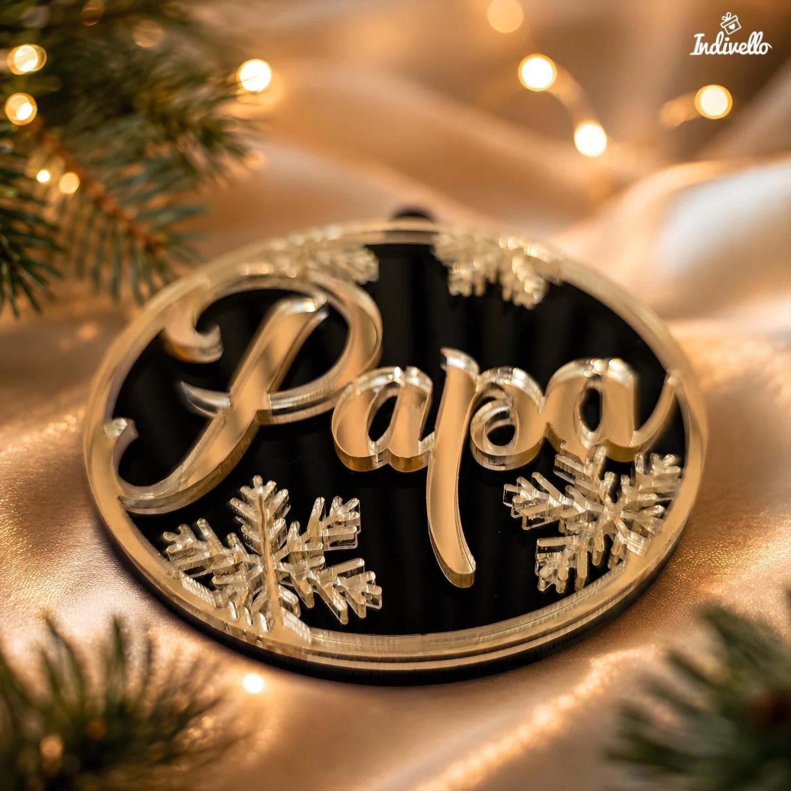 Runder, schwarz glänzender Weihnachtsanhänger mit erhabenem, golden spiegelndem Schriftzug „Papa“ und dekorativen Schneeflocken. Nahaufnahme zwischen Tannenzweigen und warmen Lichtern.