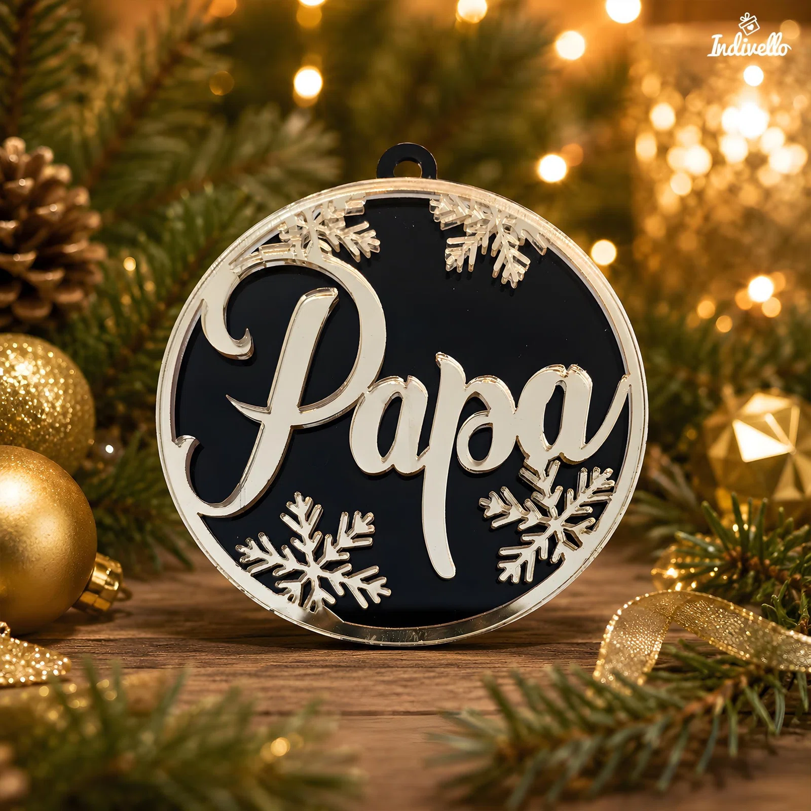 Runder Weihnachtsanhänger in Schwarz mit silberfarbener Umrandung, großer Aufschrift „Papa“ und mehreren Schneeflocken. Frontal zwischen Tannenzweigen, goldenen Kugeln und warmen Lichtern inszeniert.