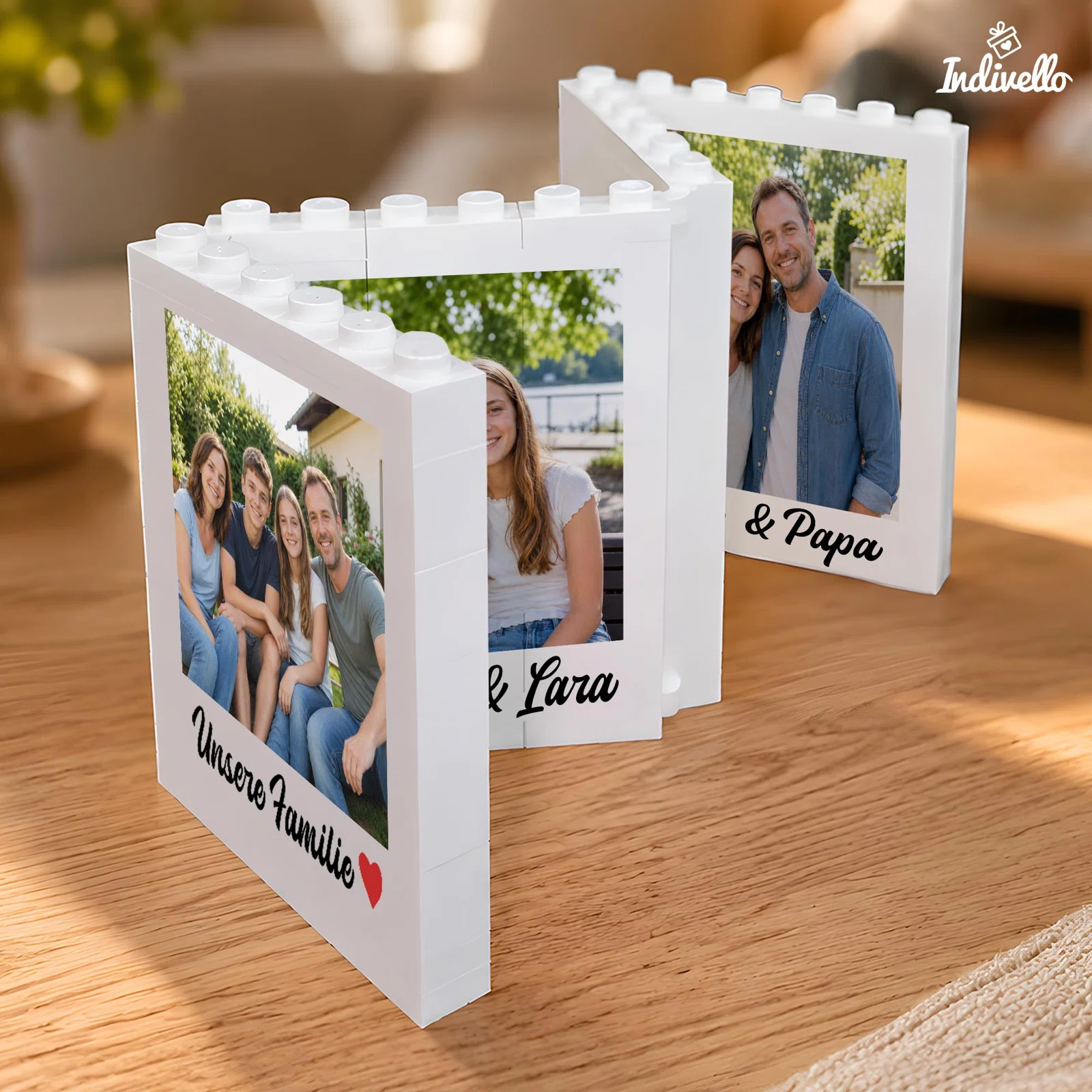 Drei weiße, rechteckige Fotorahmen in Klemmbaustein-Optik stehen versetzt auf einem Holztisch. Sie zeigen Hochformatfotos, schwarze Schreibschrift und vorne ein kleines rotes Herz.