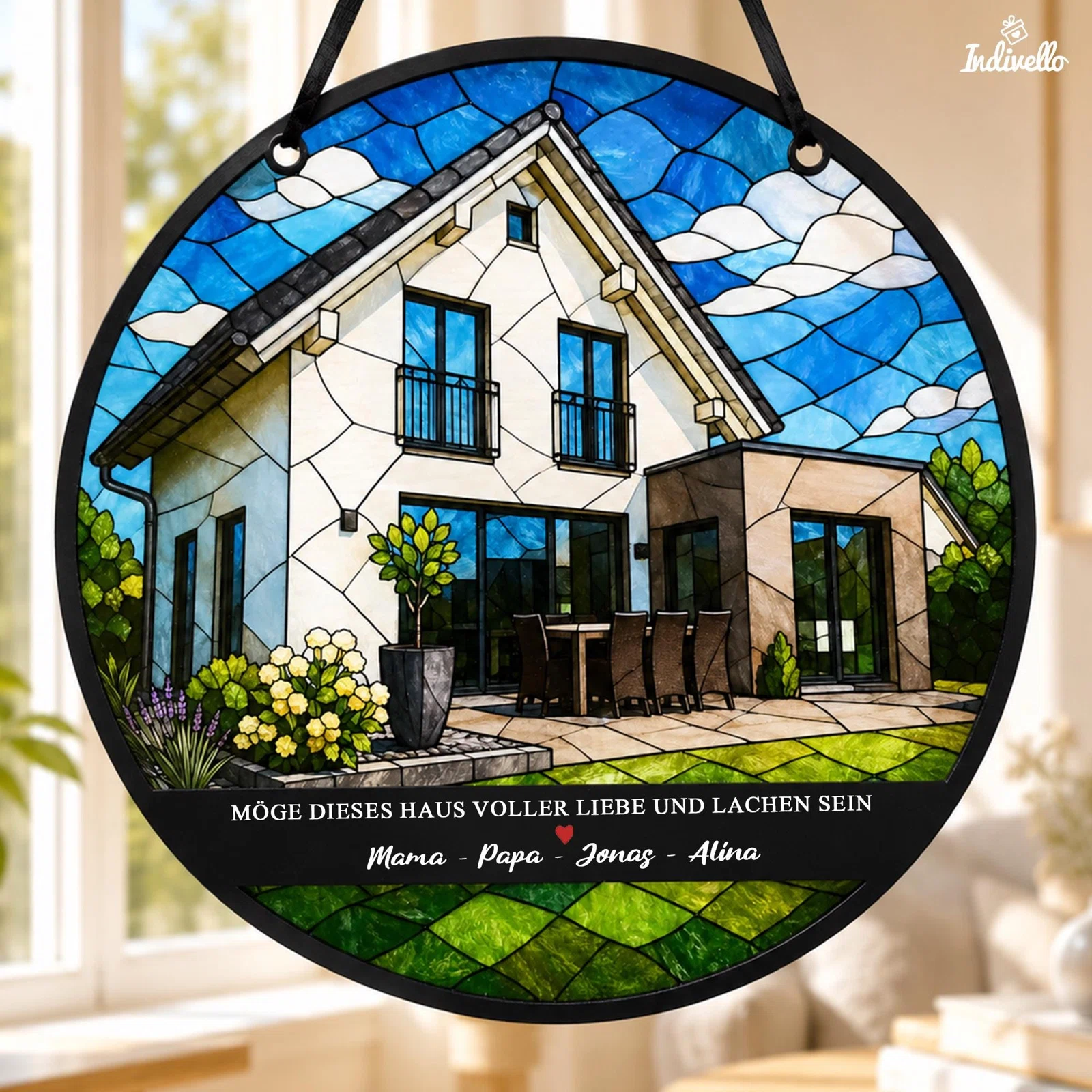 Runder Fensteranhänger in Buntglasoptik, frontal an einem schwarzen Band gezeigt, mit modernem Haus, Garten und blauem Himmel. Darunter steht „Möge dieses Haus voller Liebe und Lachen sein“ mit personalisierten Namen.