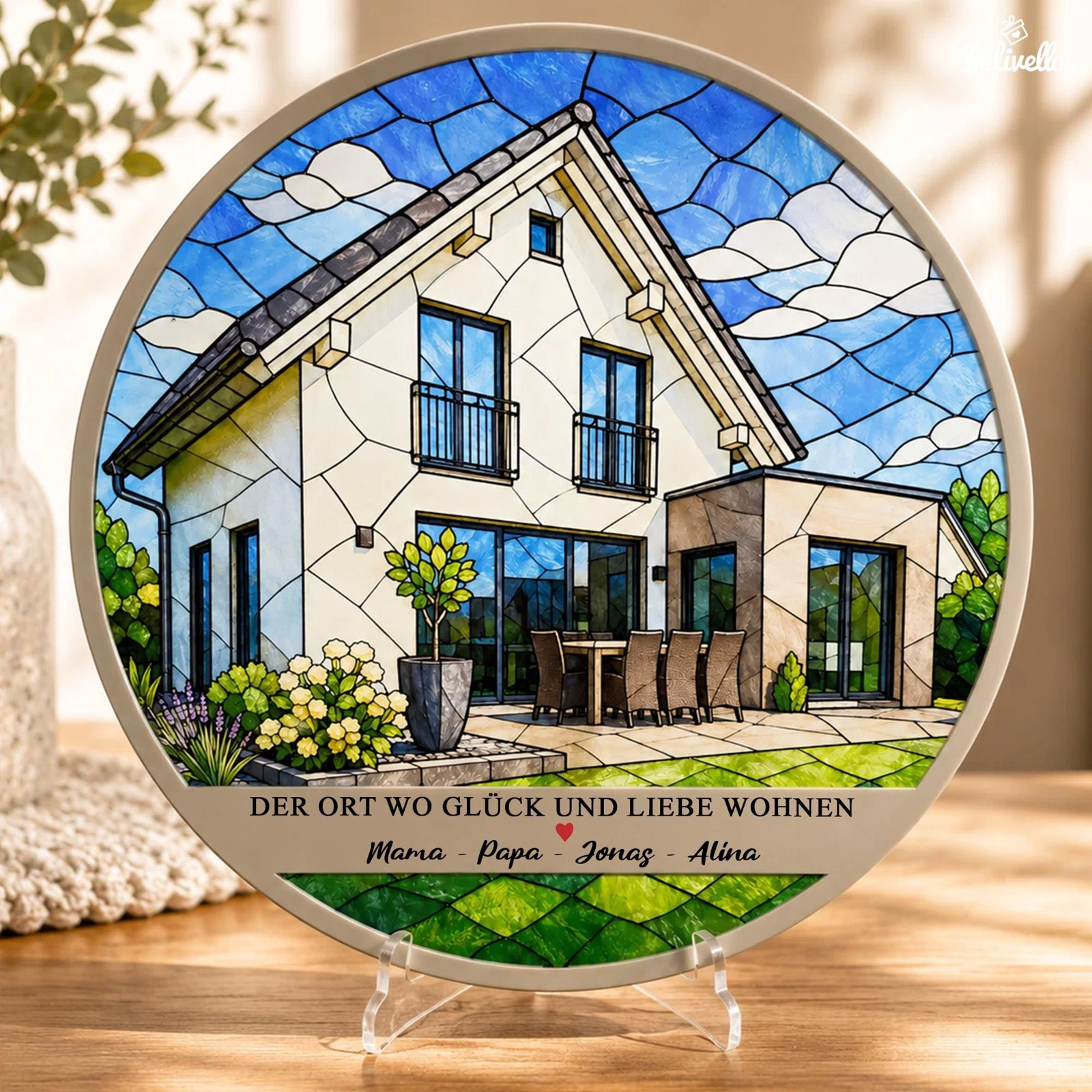 Runde Deko-Plakette auf transparentem Aufsteller, gestaltet wie ein farbiges Glasfenster: modernes Haus mit Terrasse, Garten und blauem Wolkenhimmel sowie Spruch „Der Ort, wo Glück und Liebe wohnen“ und Namenszeile.