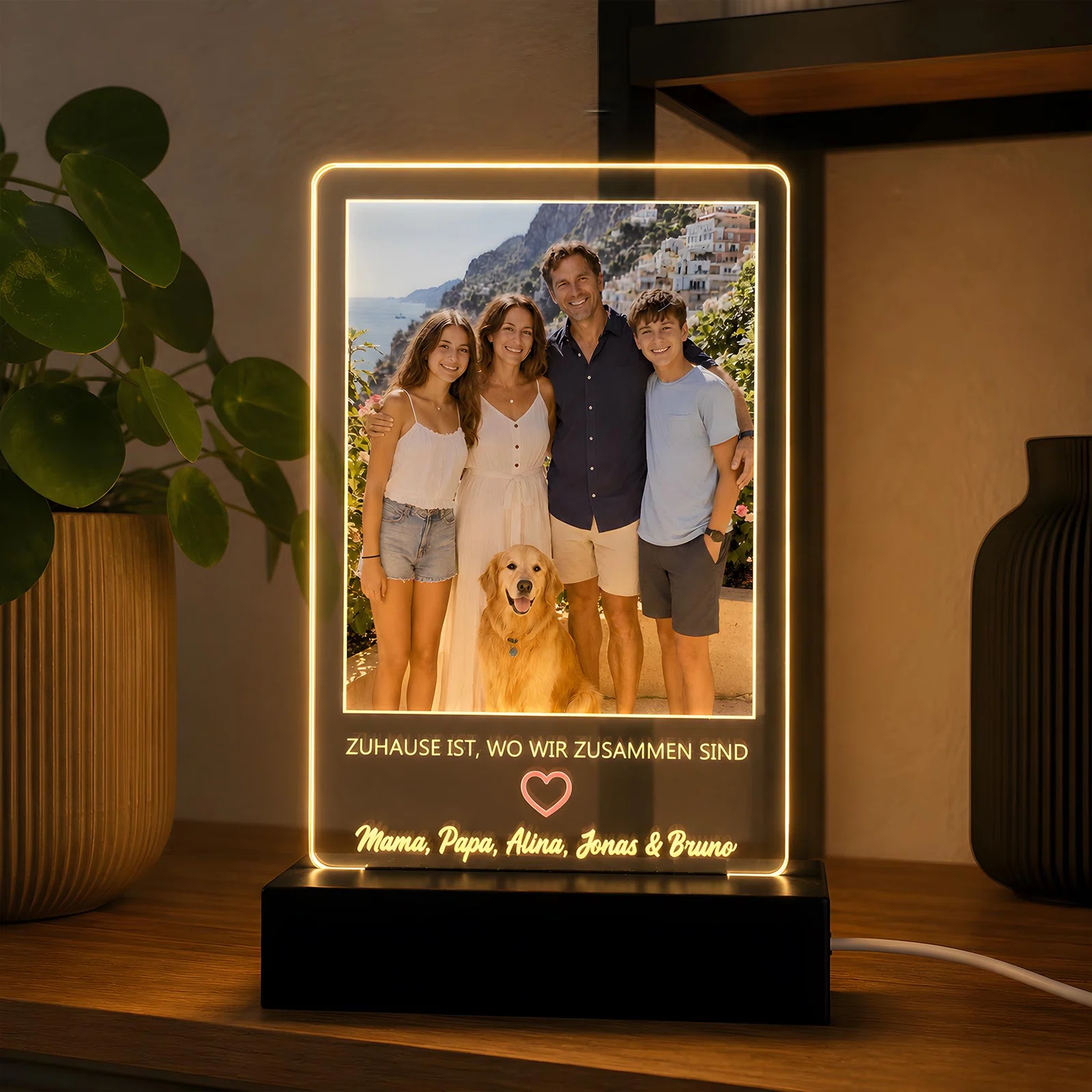 Rechteckige, personalisierte Fotoleuchte im Hochformat auf schwarzem Sockel, mit warmweiß leuchtendem Rand. Unter dem Gruppenfoto mit Hund stehen ein Zuhause-Spruch, Herzsymbol und Wunschnamen.