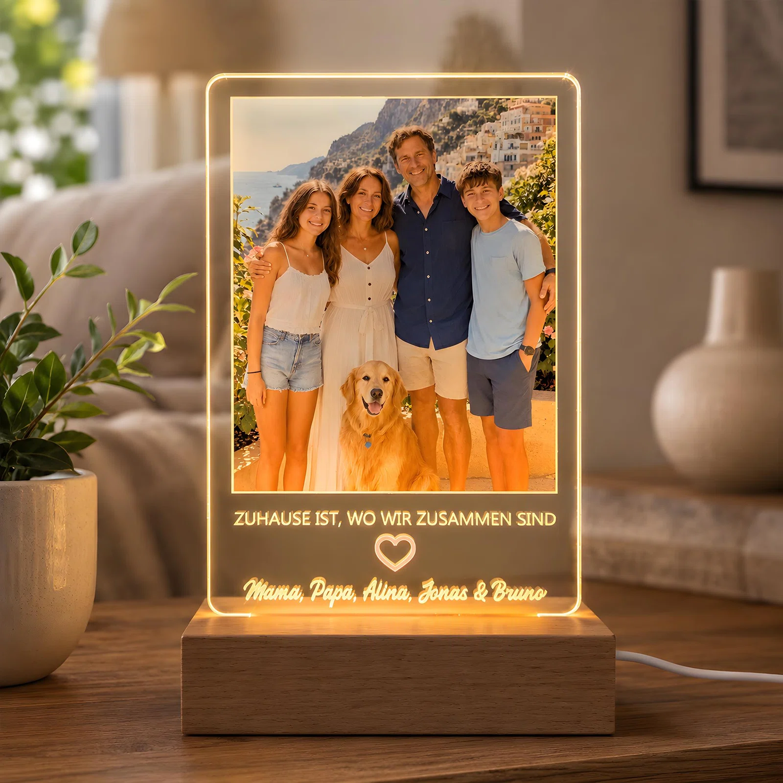 Warmweiß leuchtende, rechteckige Fototafel auf einem Holzsockel, frontal auf einem Tisch. Zu sehen sind vier Personen mit Hund, ein Herzsymbol und der Spruch „Zuhause ist, wo wir zusammen sind“.