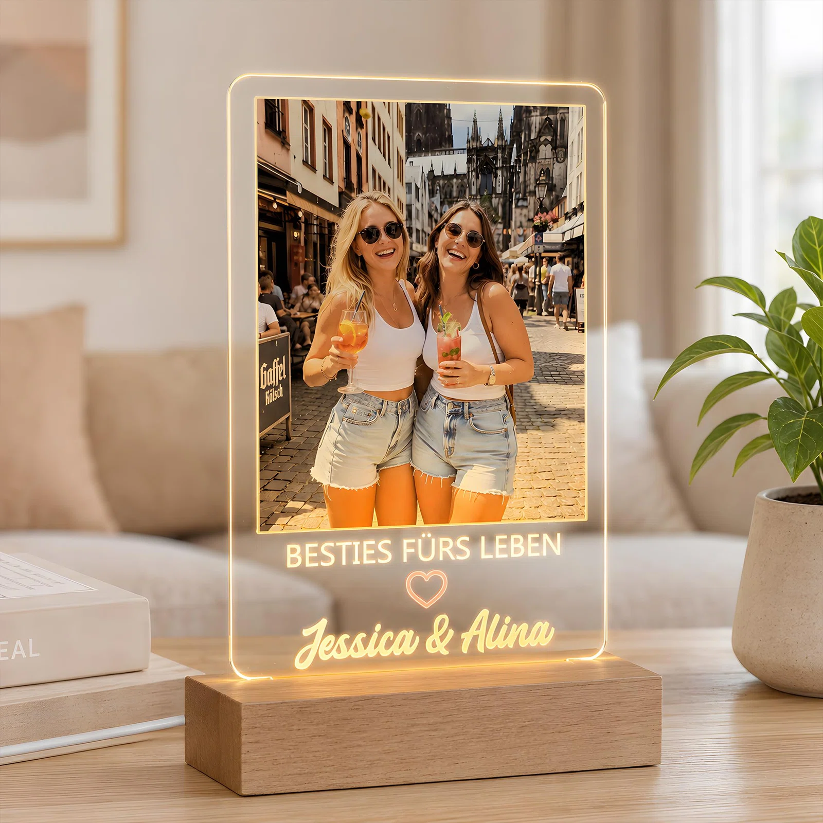Rechteckige, transparent leuchtende Fototafel auf einem Sockel in Holzoptik, frontal fotografiert. Sie zeigt zwei Personen mit Sonnenbrillen und Getränken sowie den Spruch „Bestes fürs Leben“, Herz und zwei Namen.