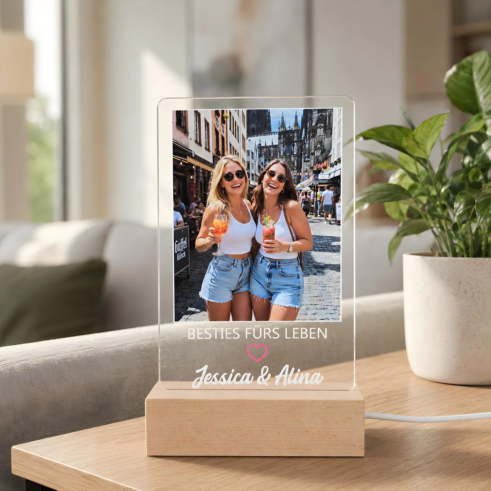 Personalisierbare rechteckige Fotoleuchte in transparentem Design auf hellem Sockel in Holzoptik. Frontalansicht mit Foto zweier Frauen, Schriftzug „Besties fürs Leben“ und rosa Herz.