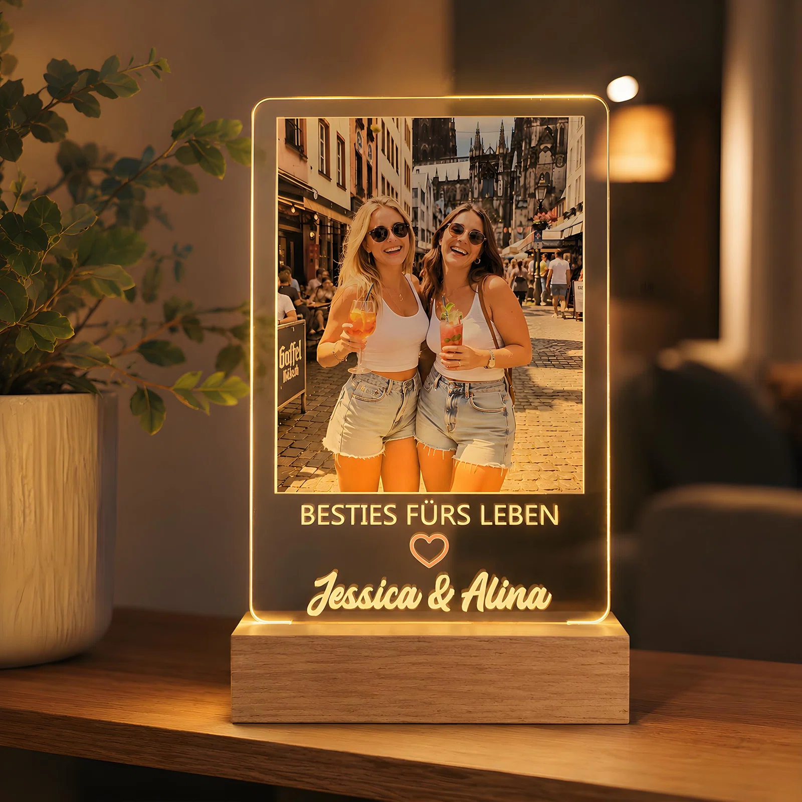 Rechteckige, transparente Fotoplatte im Sockel mit warm leuchtendem Rand, frontal fotografiert. Das Stadtfoto zweier Personen wird durch den Spruch „Besties fürs Leben“, ein Herz und Namen ergänzt.
