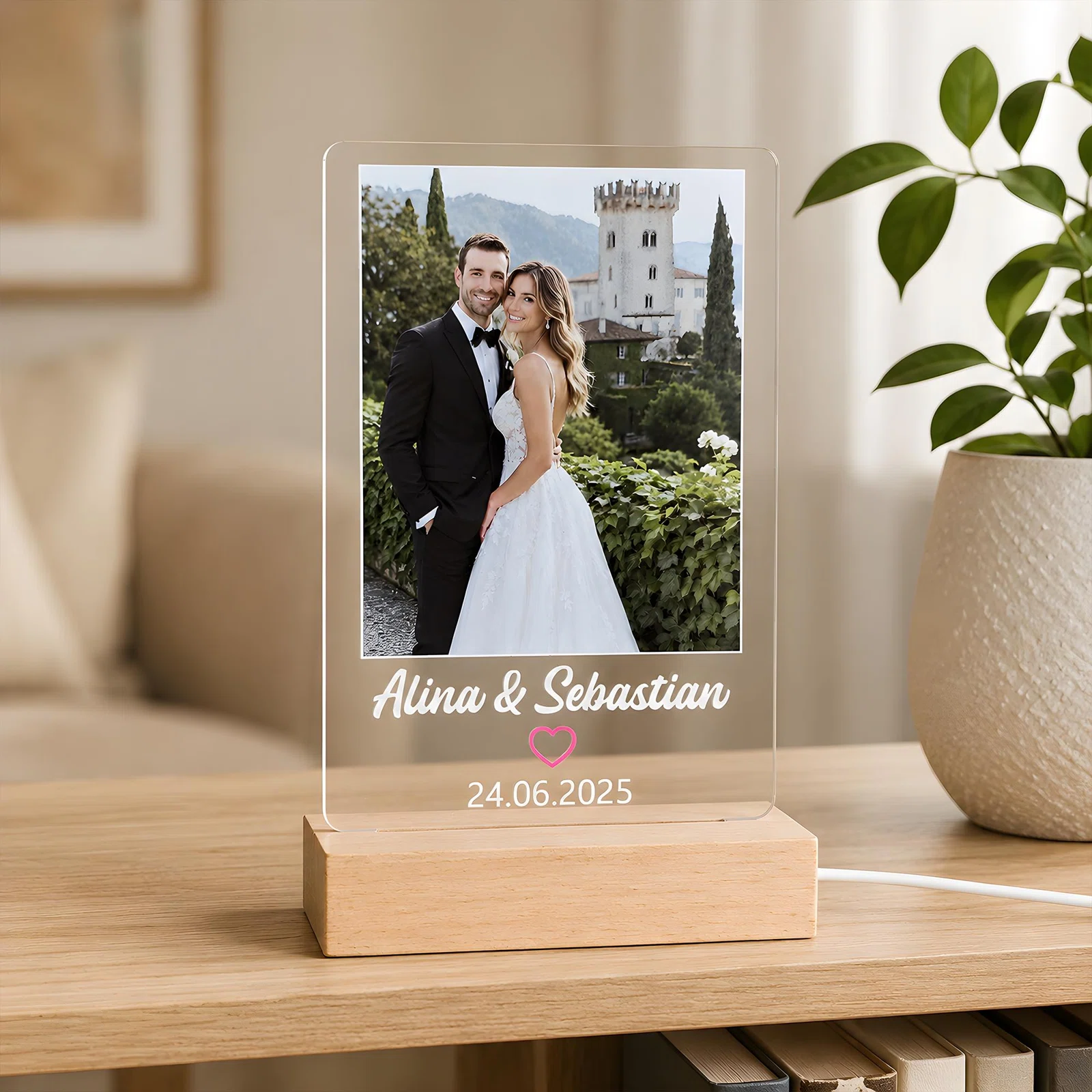 Beleuchtete, transparente Fototafel im Hochformat mit Bild zweier festlich gekleideter Personen vor einem Schloss. Darunter stehen zwei Namen, ein rosa Herz und ein Datum.