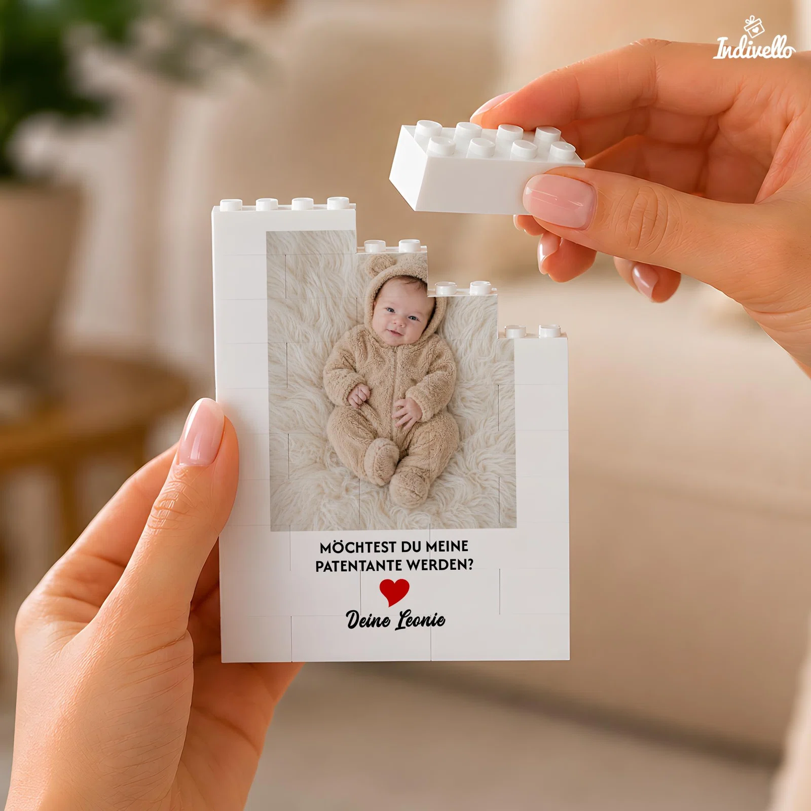 Weiße Fototafel in Klemmbaustein-Optik mit Babybild, der Frage „Möchtest du meine Patentante werden?“ und rotem Herz. Zwei Hände setzen einen weißen Baustein auf die Oberkante.