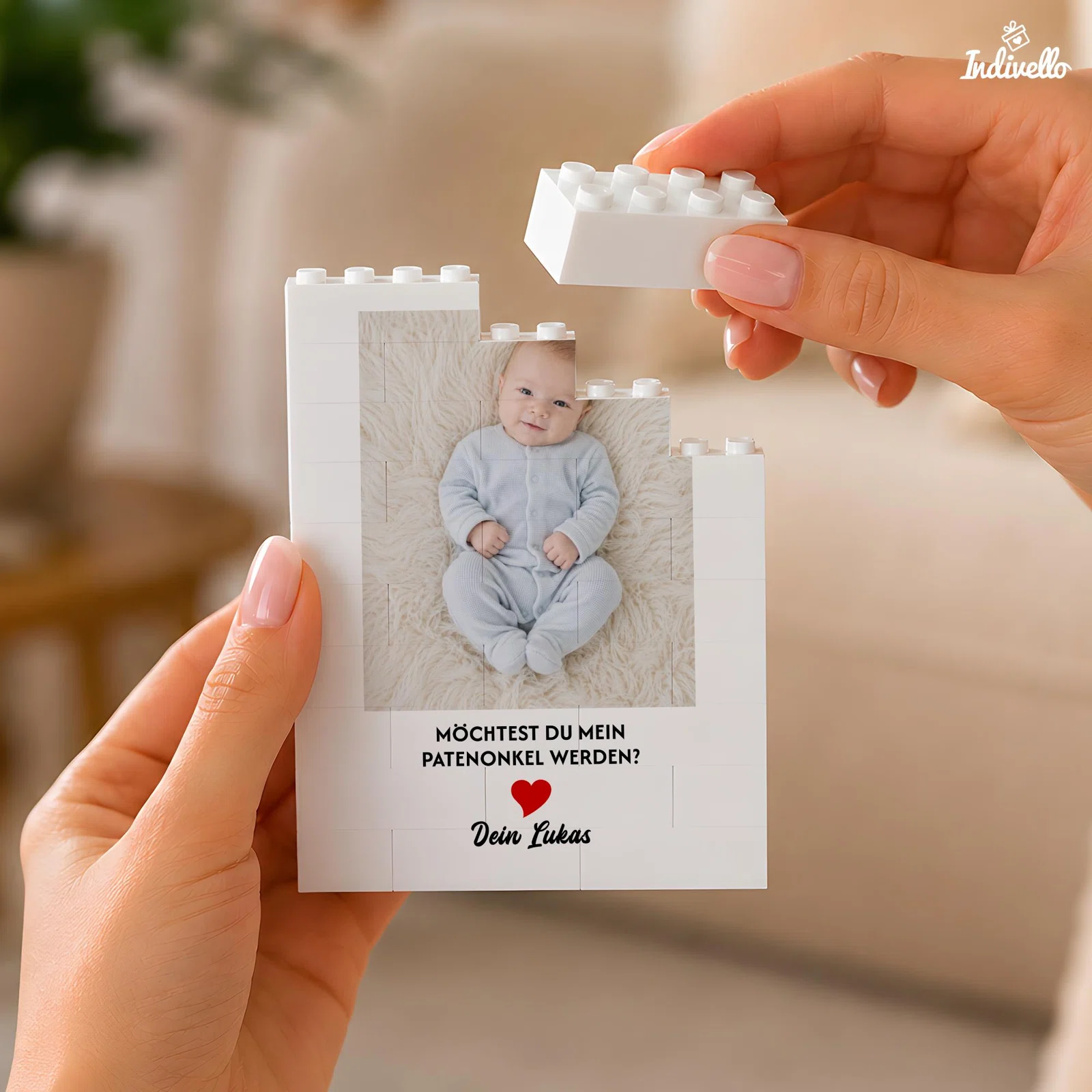 Weiße Karte aus zusammensteckbaren Bausteinen mit Babyfoto, rotem Herz und der Frage „Möchtest du mein Patenonkel werden?“. Zwei Hände setzen den oberen Baustein auf.