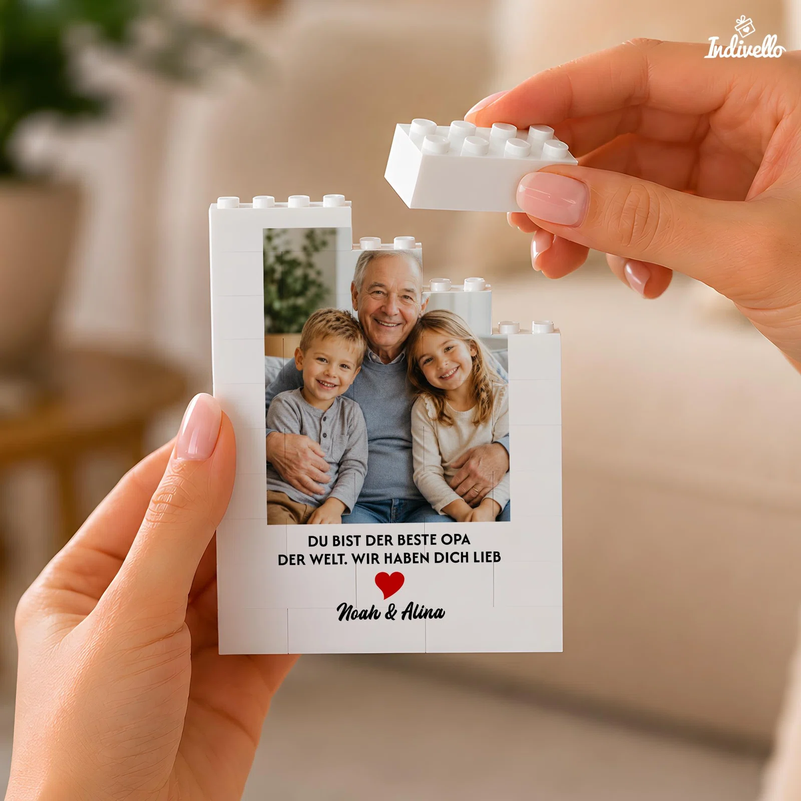 Weißer Fotorahmen aus Klemmbausteinen mit Porträt eines älteren Mannes und zweier Kinder, rotem Herz und Opa-Spruch. Zwei Hände halten den Rahmen und setzen oben einen weißen Stein auf.