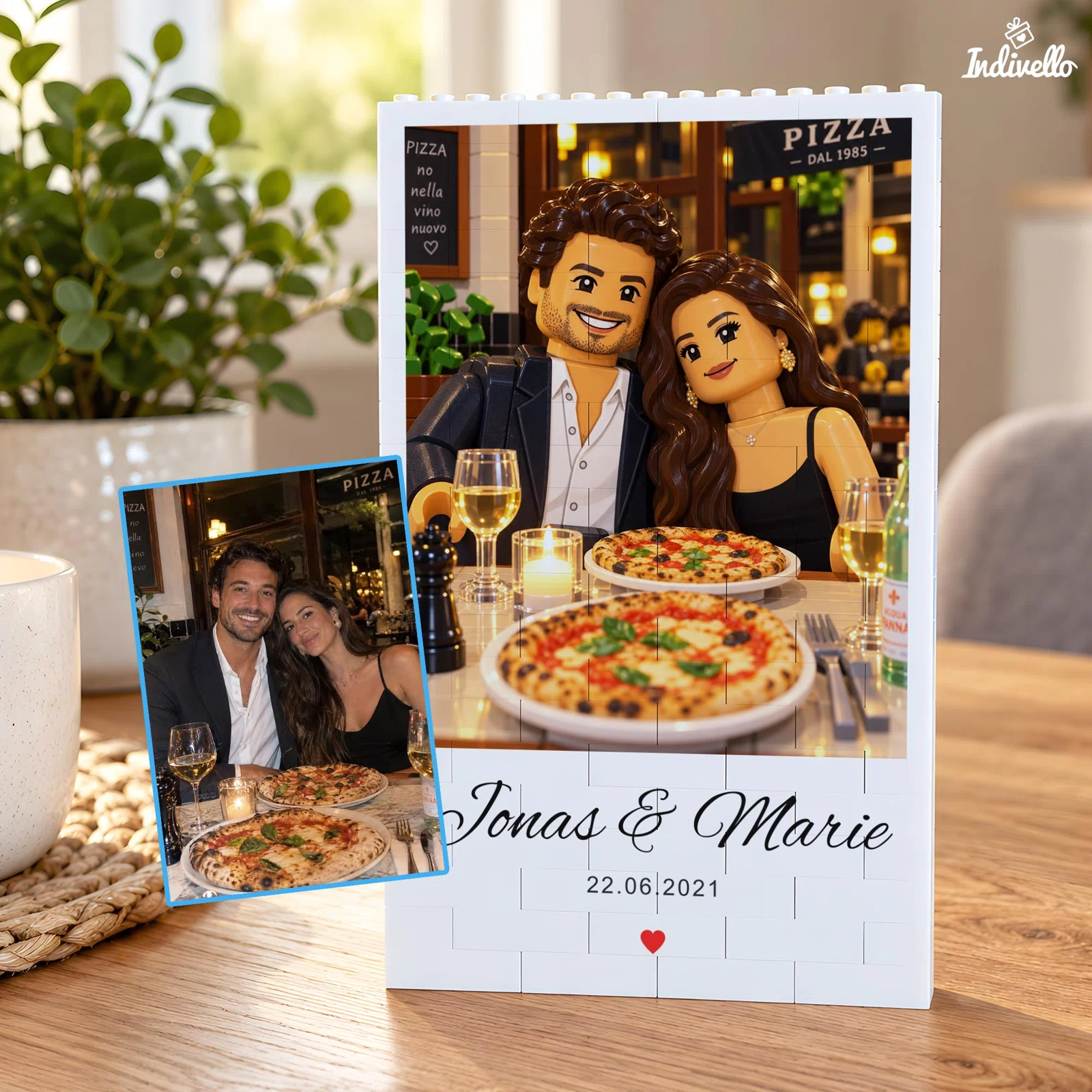 Hochformatiges, personalisiertes Klemmbaustein-Porträt eines Paares beim Pizzaessen, mit Namen, Datum und rotem Herz auf weißem Sockel; daneben steht die farbige Fotovorlage.