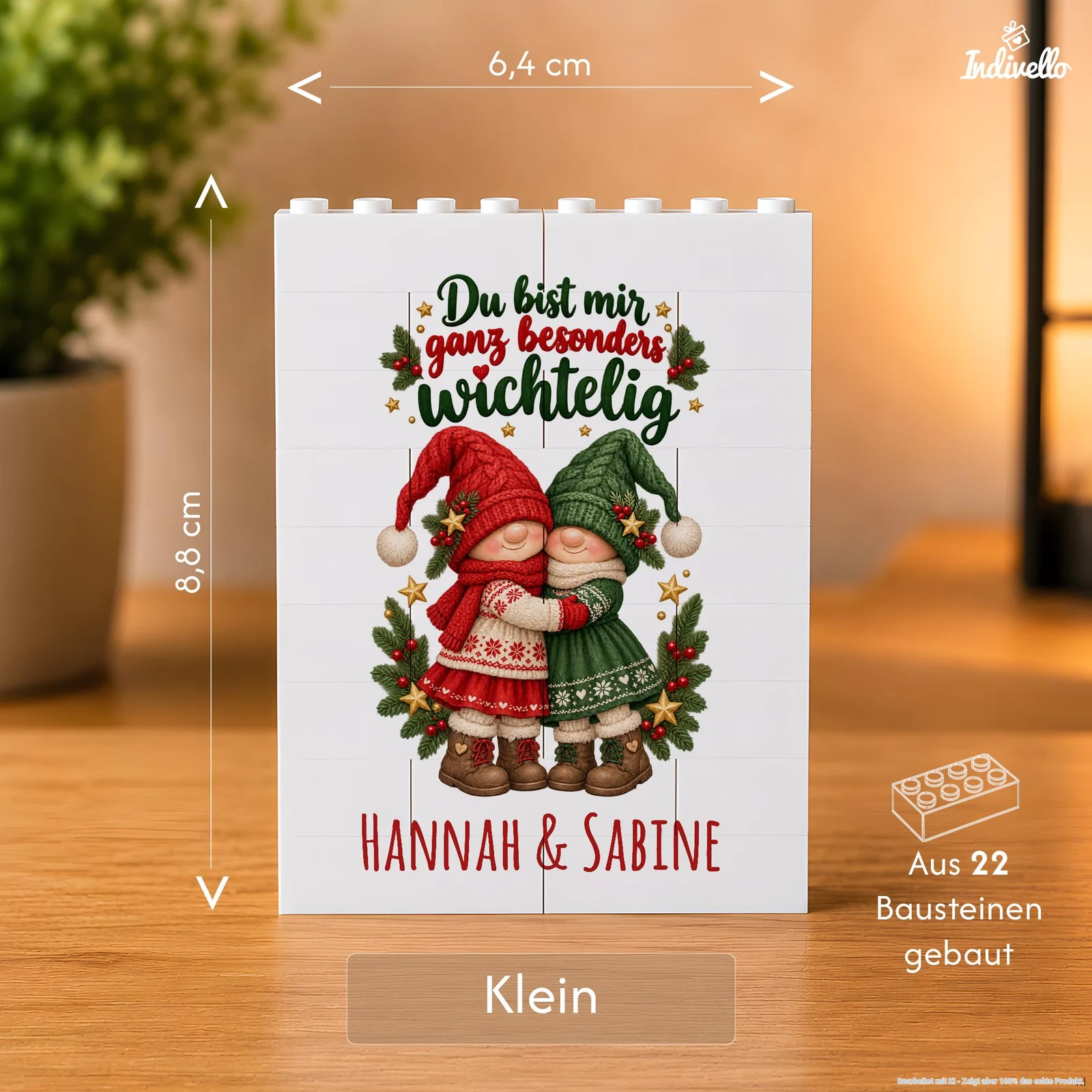 Frontalansicht einer kleinen weißen Deko-Tafel aus 22 Bausteinen auf einem Holztisch. Das Weihnachtsmotiv zeigt zwei sich umarmende Wichtel in Rot und Grün mit Tannenzweigen sowie den Aufschriften „Du bist mir ganz besonders wichtelig“ und „Hannah & Sabine“.