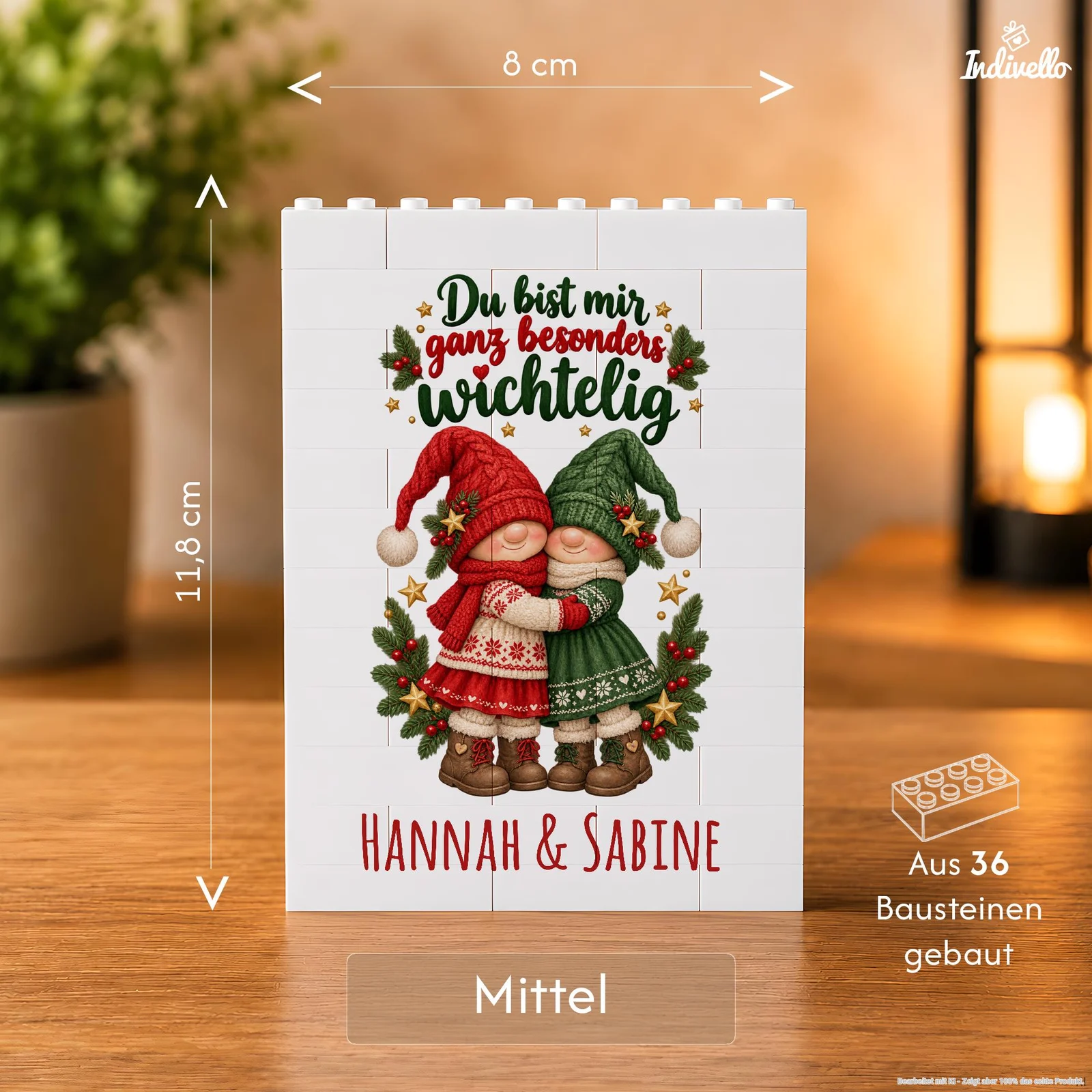 Frontalansicht einer weißen Baustein-Tafel mit zwei sich umarmenden Weihnachtswichteln in Rot und Grün, Tannenzweigen und Sternen. Darüber steht „Du bist mir ganz besonders wichtelig“, darunter „Hannah & Sabine“; die Infografik kennzeichnet die Größe als „Mittel“ und nennt 36 Bausteine.