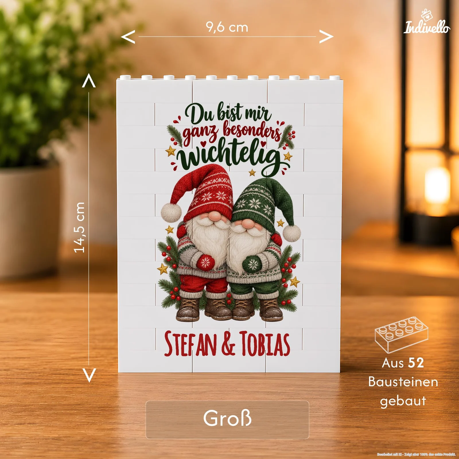 Frontale Ansicht einer weißen Baustein-Tafel auf einem Holztisch, bedruckt mit zwei Weihnachtswichteln in Rot und Grün, Tannenzweigen und Sternen. Darauf stehen „Du bist mir ganz besonders wichtelig“ und „Stefan & Tobias“; die Grafik weist zudem auf 52 Bausteine hin.
