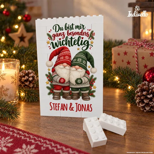 Frontal gezeigte weiße Klemmbaustein-Tafel mit zwei Weihnachtswichteln in Rot und Grün, Tannenzweigen und dem Spruch „Du bist mir ganz besonders wichtig“ sowie „Stefan & Jonas“. Sie steht auf einem Holztisch zwischen Kerze, Lichterketten, Tannengrün, Geschenk und Zapfen; lose weiße Bausteine liegen davor.
